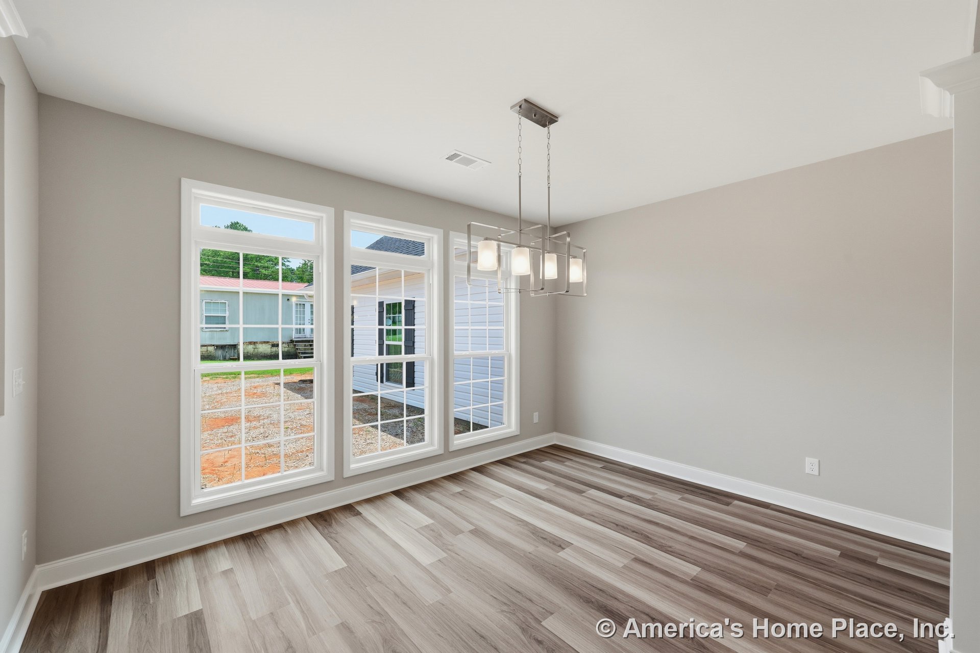 Dining area with expansive grid windows, modern pendant light fixture, wood-look vinyl plank flooring, neutral wall paint, white baseboards, and rectangular room layout.