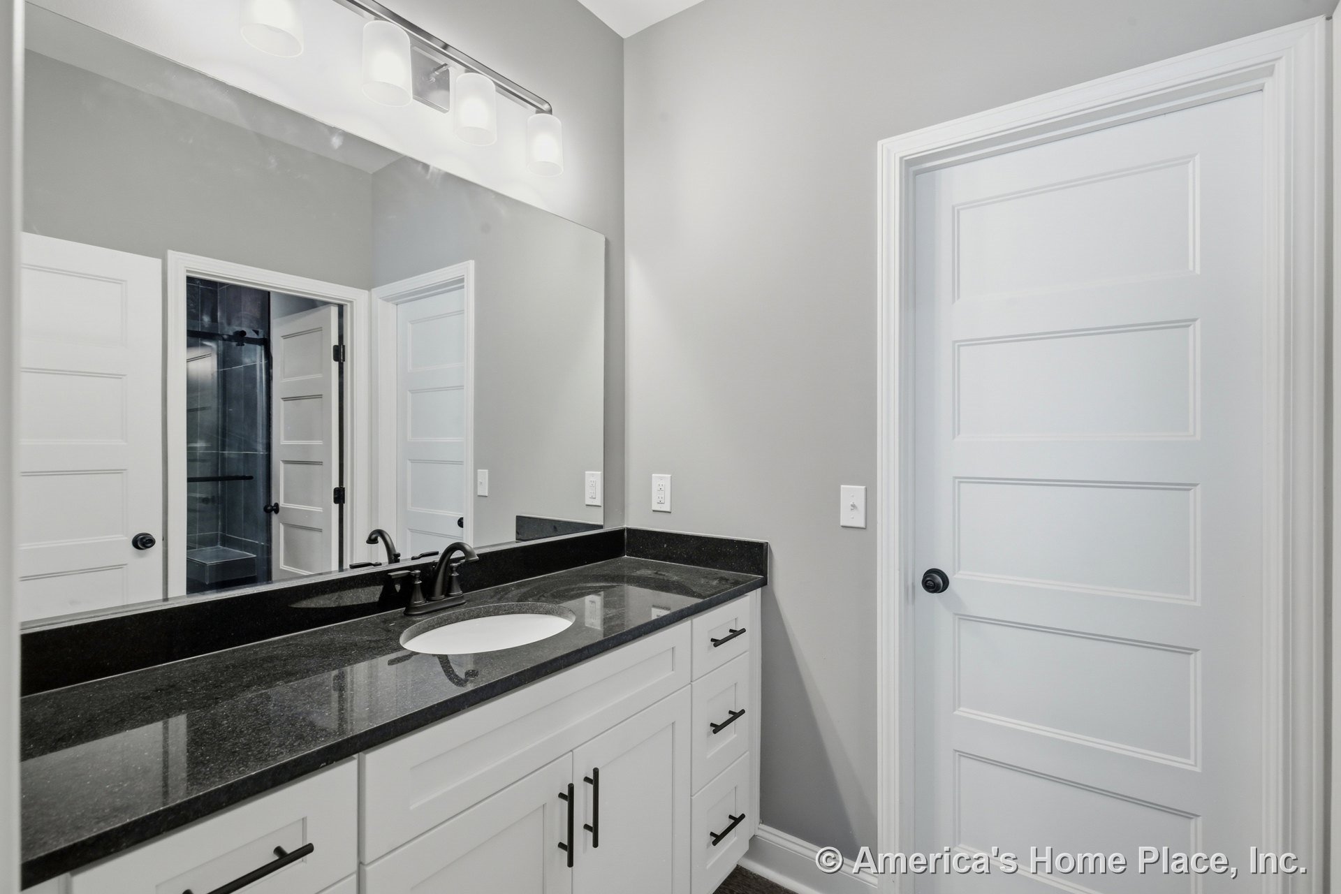 Black stone vanity top with built-in sink, white shaker cabinets, large wall mirror, modern vanity light fixture, matte black faucet, panel interior doors, neutral wall color, and