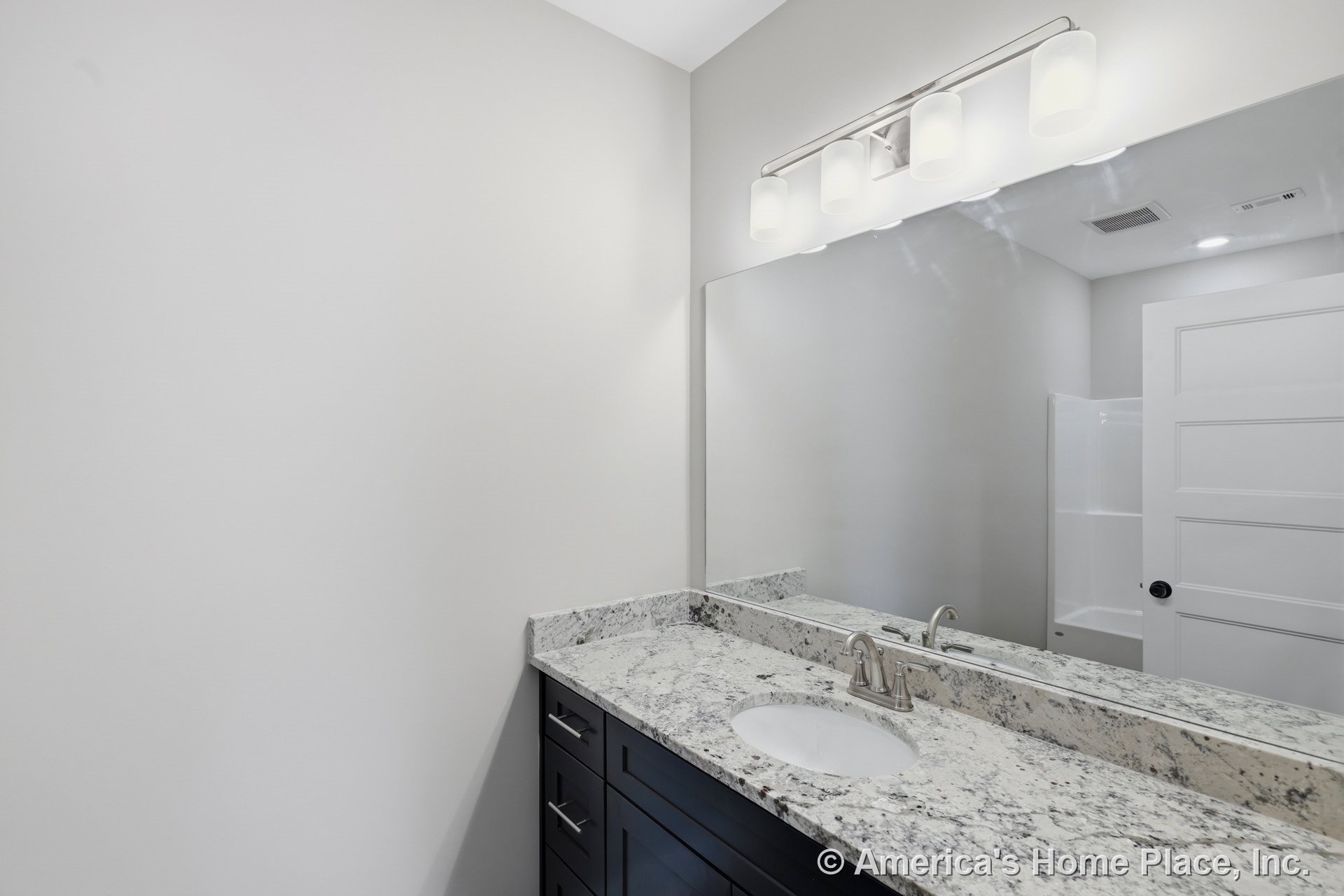 Granite vanity countertop with undermount sink, dark shaker cabinets, large wall mirror, modern vanity light fixture, white paneled door, and neutral wall color.