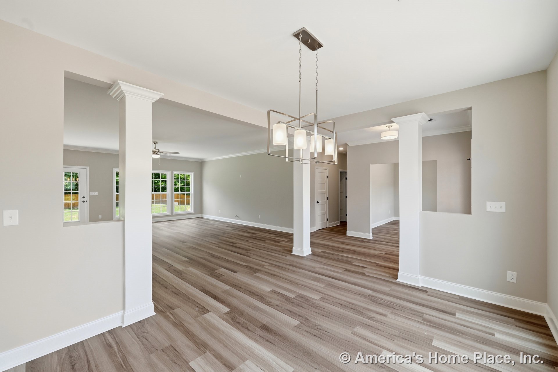 Open concept living and dining area with wide plank wood-look vinyl flooring, large windows framed in white trim, modern chandelier and recessed ceiling lights, white interior
