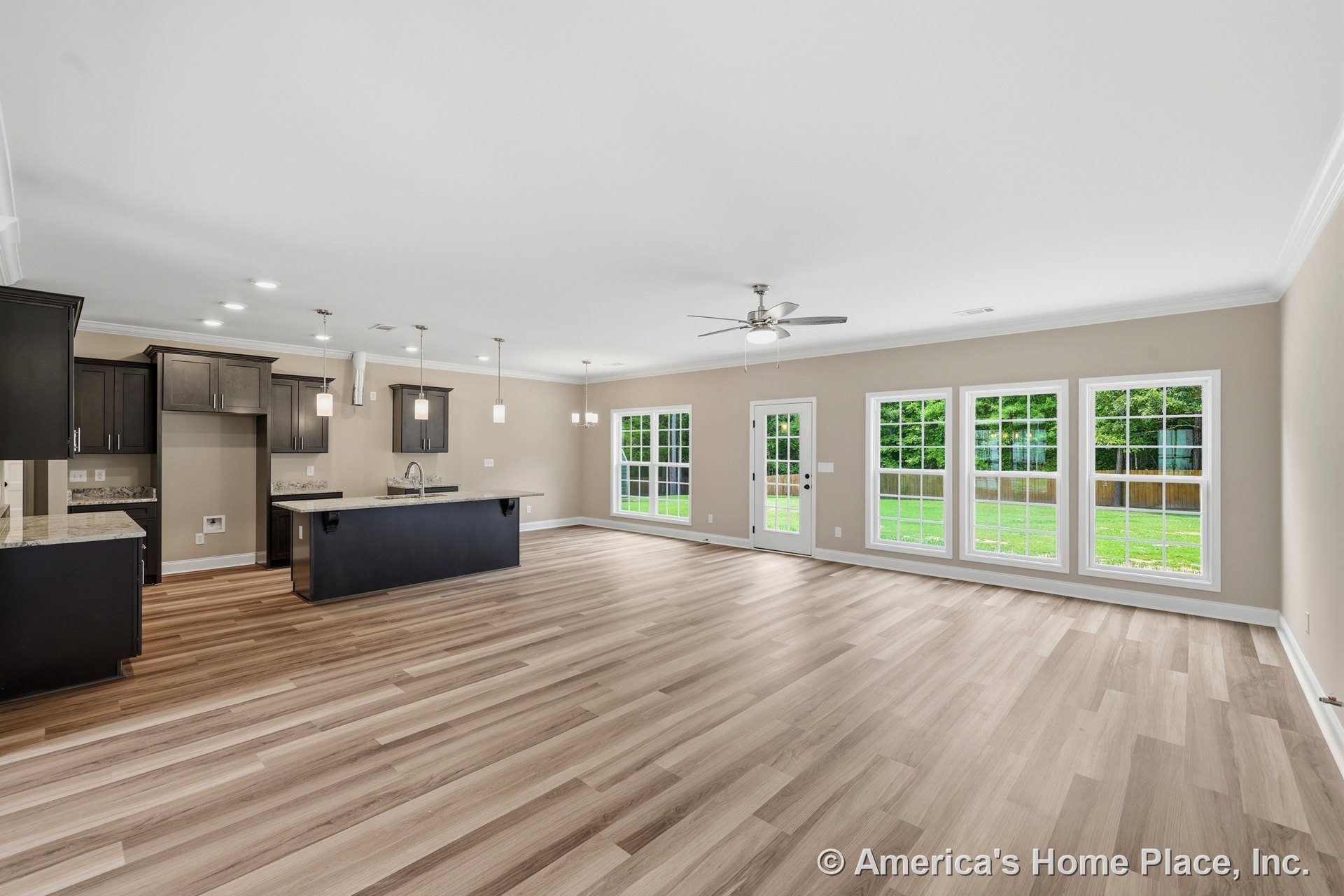 Open concept living area with expansive windows, light wood plank flooring, modern kitchen featuring dark cabinetry, granite countertops, pendant and recessed lighting, ceiling