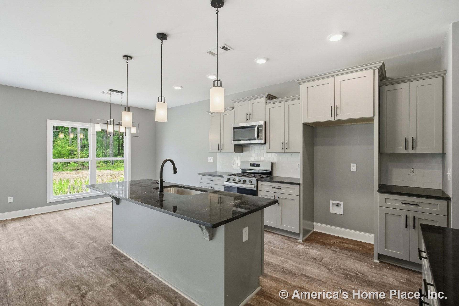 Shaker-style cabinetry with black stone countertops, central kitchen island beneath pendant lighting, stainless steel appliances, wood-look flooring, tile backsplash, window, and