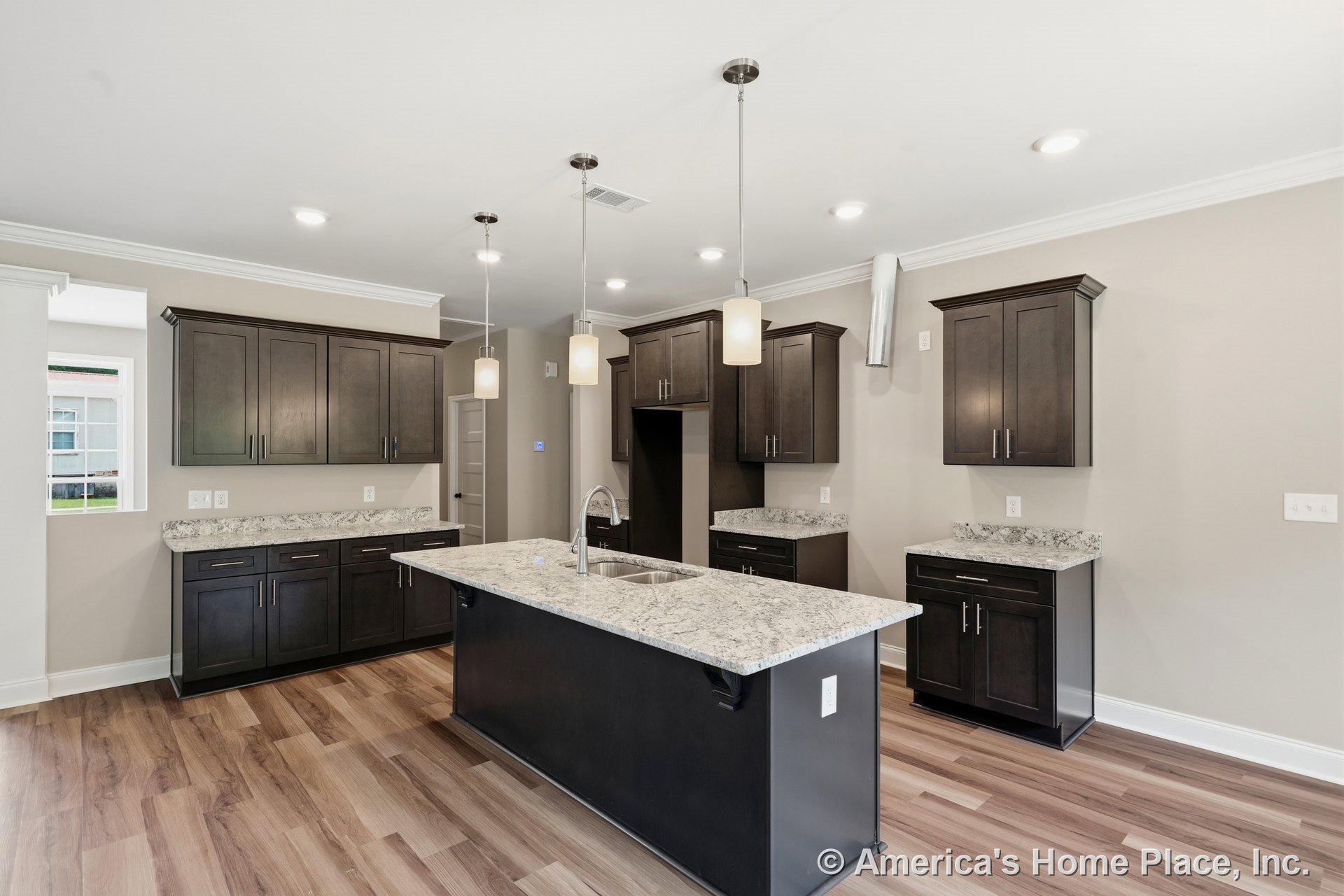 Dark wood kitchen cabinets with granite countertops, central island beneath pendant ceiling lights, wood-look flooring, white crown molding, stainless steel sink, recessed