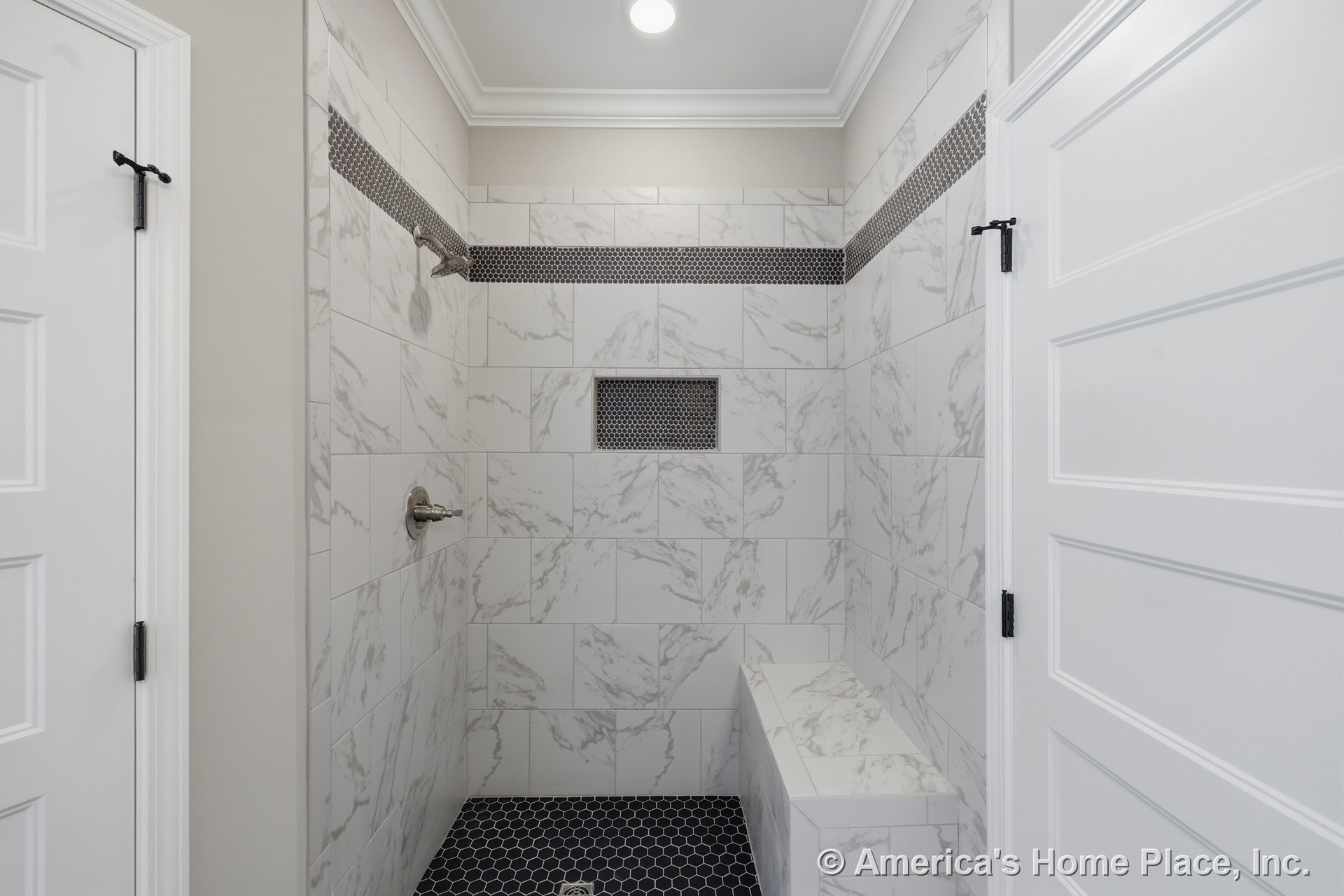 Shower with marble-look wall tile, hexagonal black floor tile, built-in bench, accent tile niche, recessed ceiling light, white paneled doors, and crown molding.