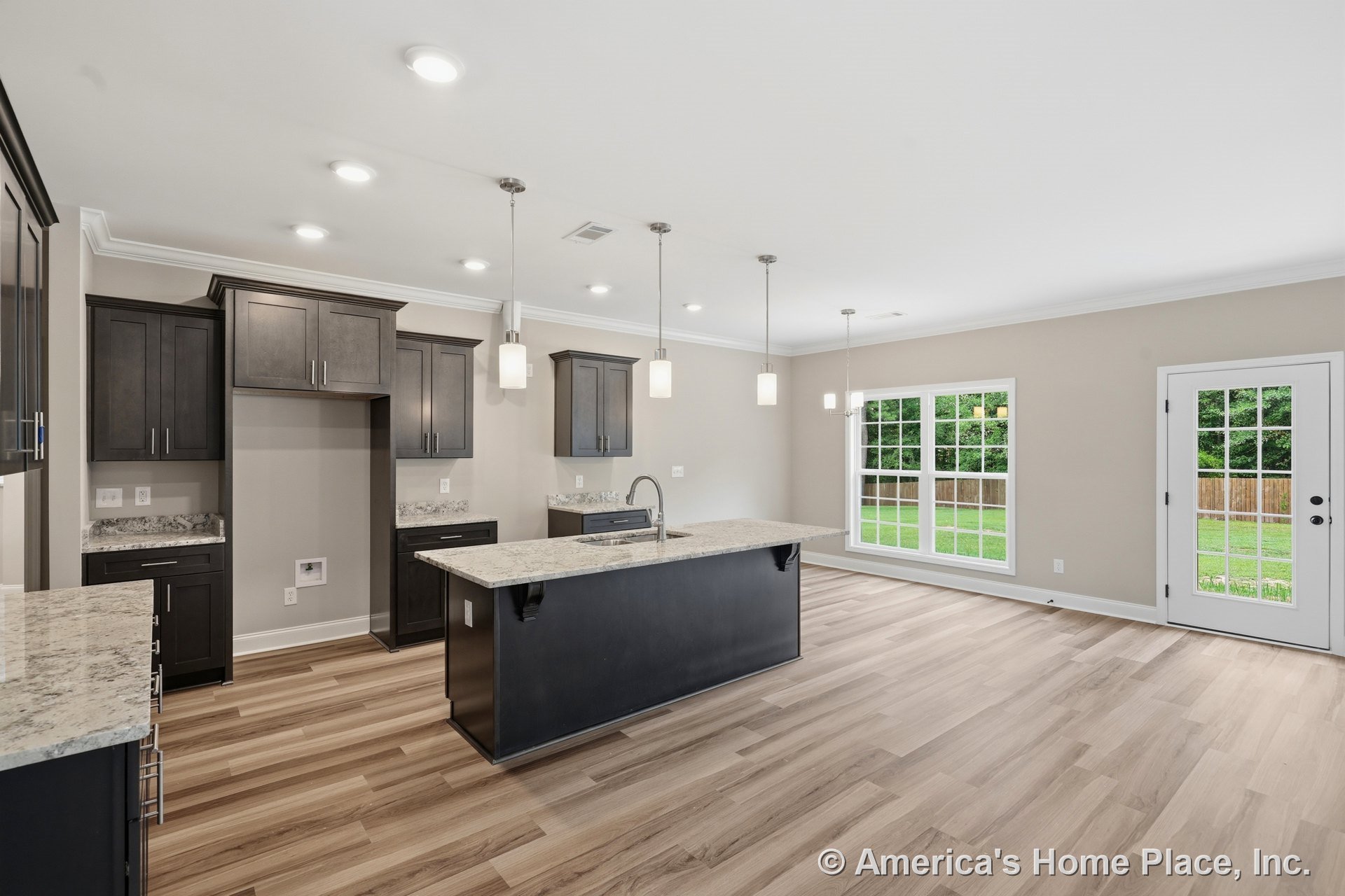 Dark wood kitchen cabinets with granite countertops, pendant lighting above island, open layout connecting to dining area, large windows, wood-look flooring, white trim and crown