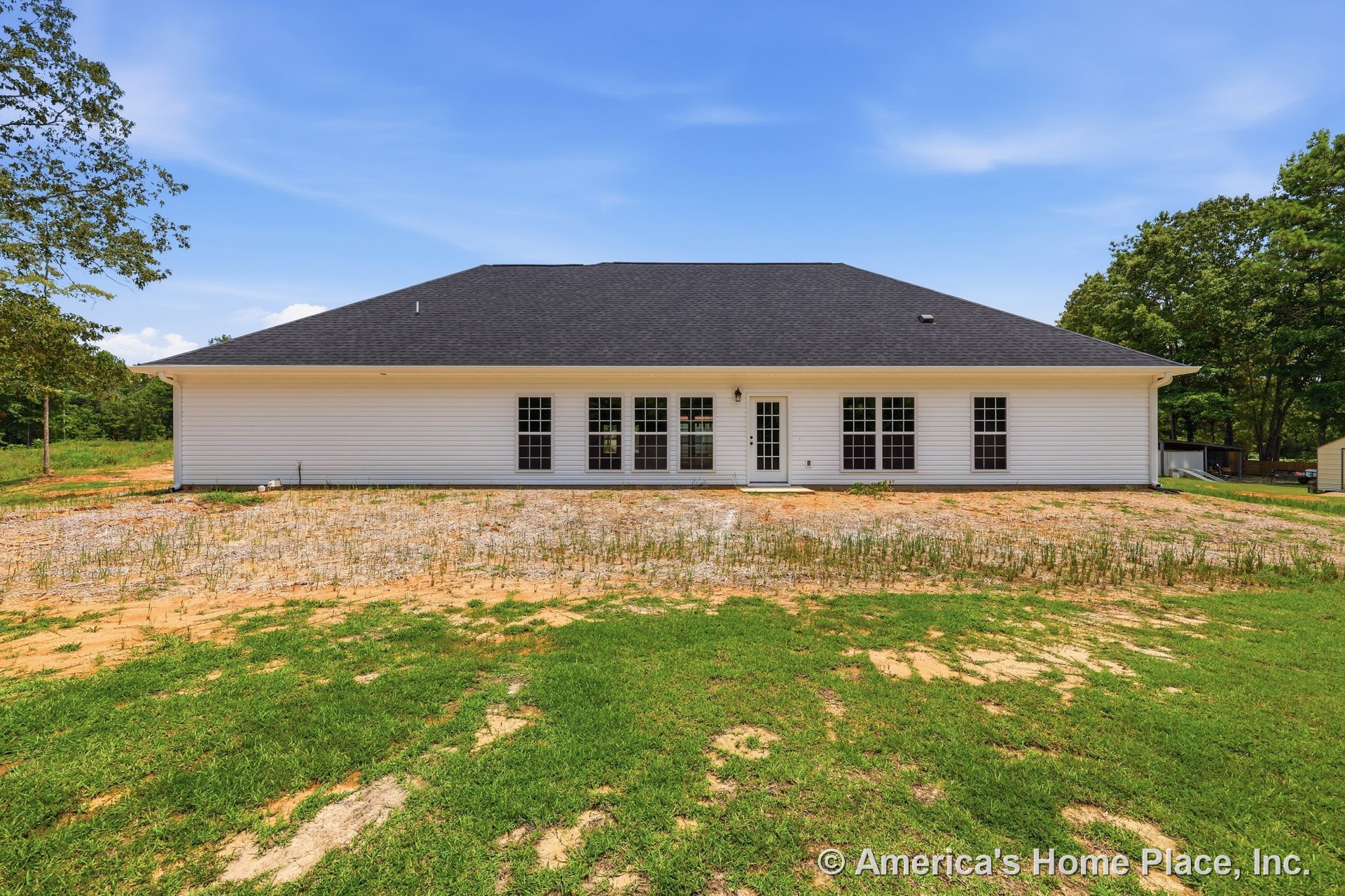 Rear elevation showcasing white horizontal siding, black shingle roof, multiple large grid windows, single exterior door, and outdoor lighting fixture.