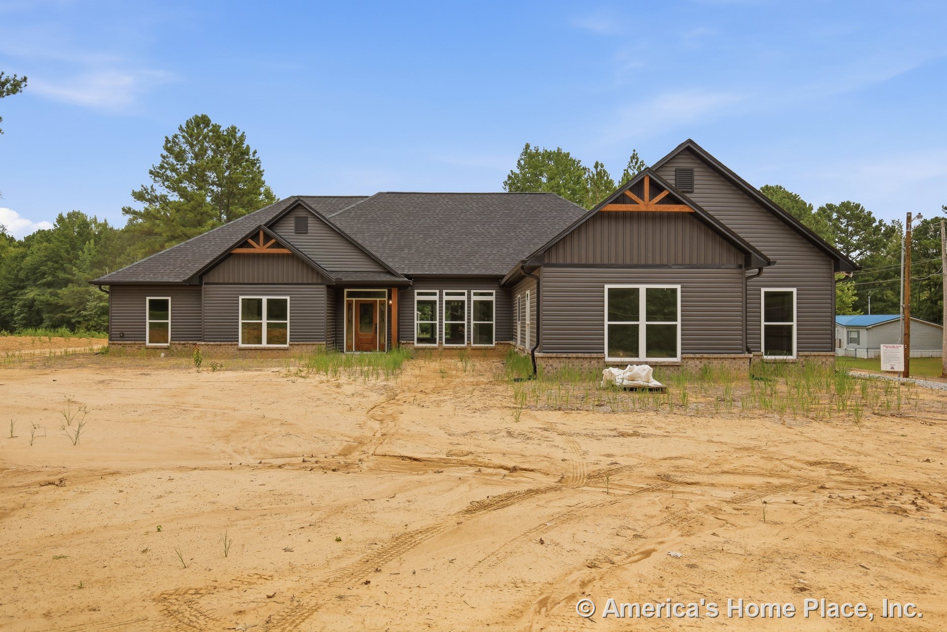 Dark gray horizontal siding with multiple gables featuring wood trim accents, large windows, covered entry porch, and brick foundation on new residential construction.