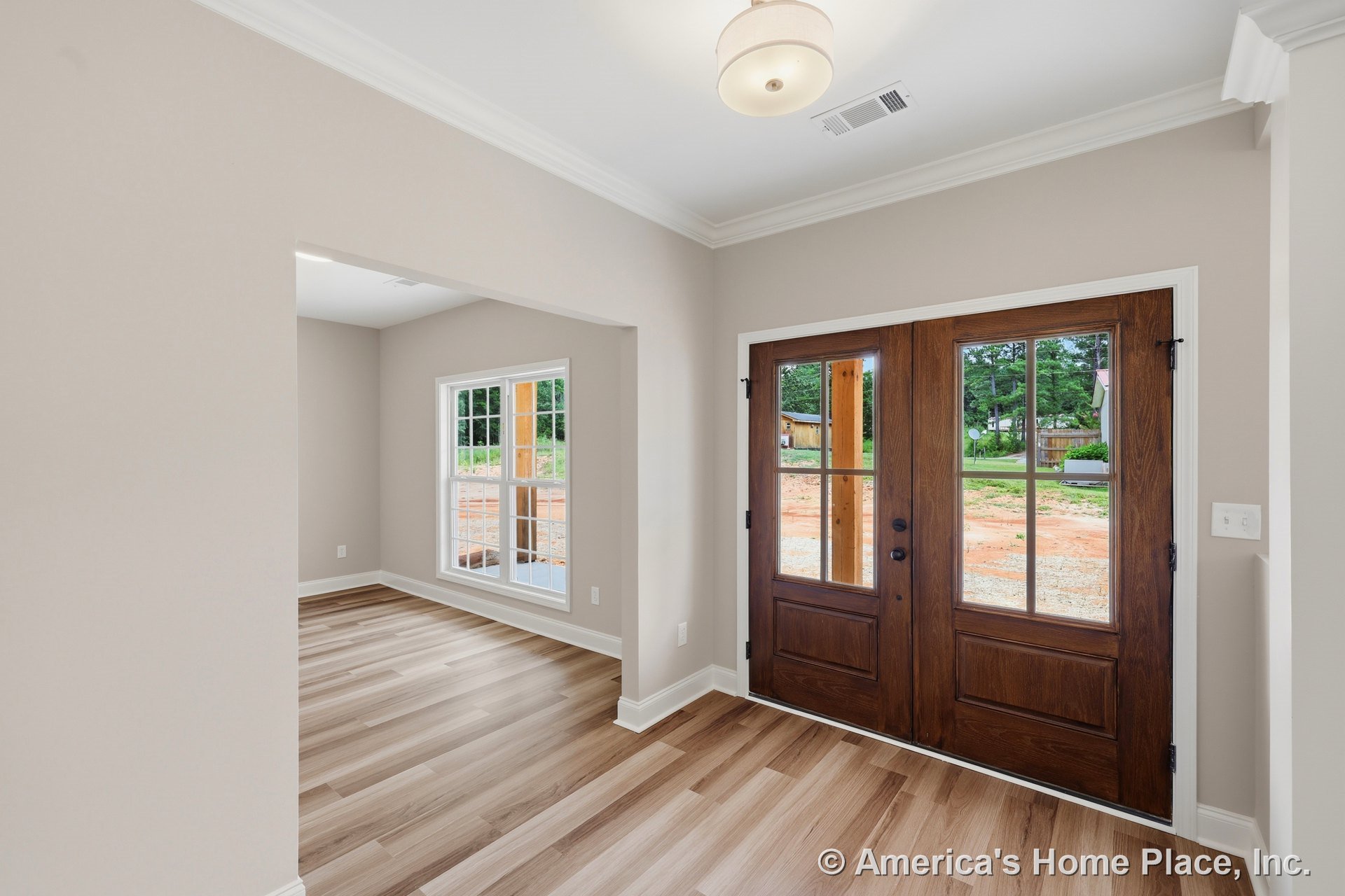Double glass-paneled wooden doors open to a foyer with light wood plank flooring, white crown molding, large front window, neutral wall paint, ceiling-mounted light fixture, and