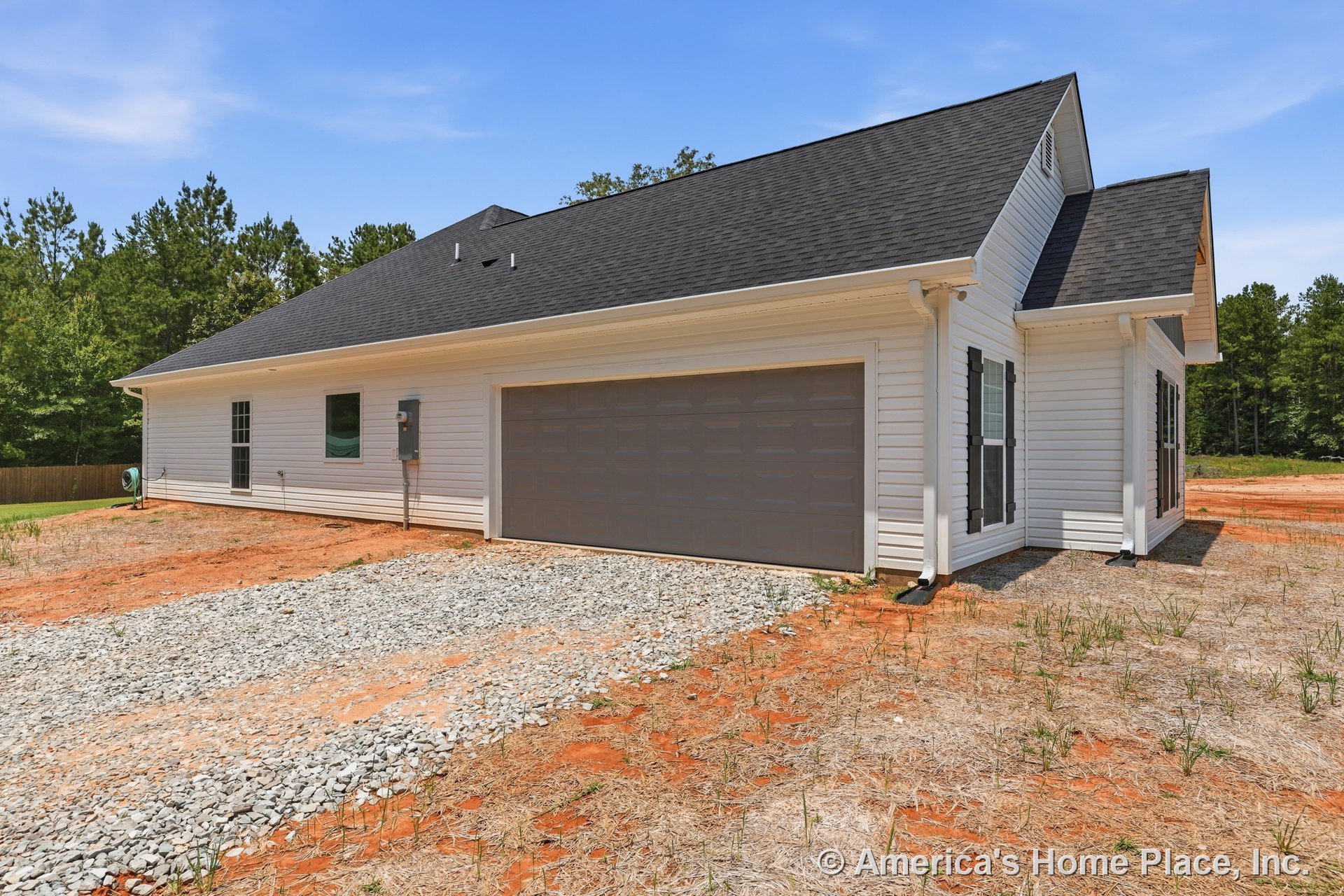 Two-car garage with double doors, light vinyl siding, black asphalt shingle roof, gravel driveway, white trim, exterior windows with shutters, porch lighting, gutters, and utility