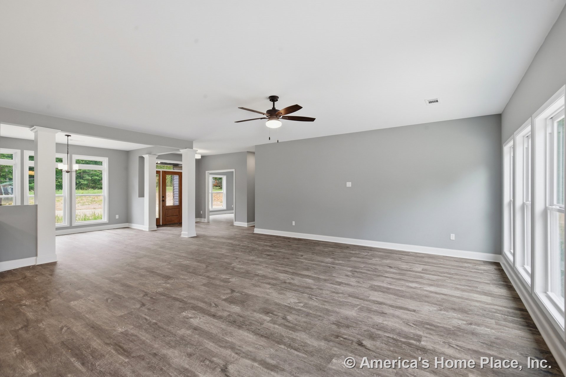 Open concept living and dining area with multiple large windows, gray painted walls, wood-look vinyl flooring, white trim and columns, ceiling fan with light, recessed lighting