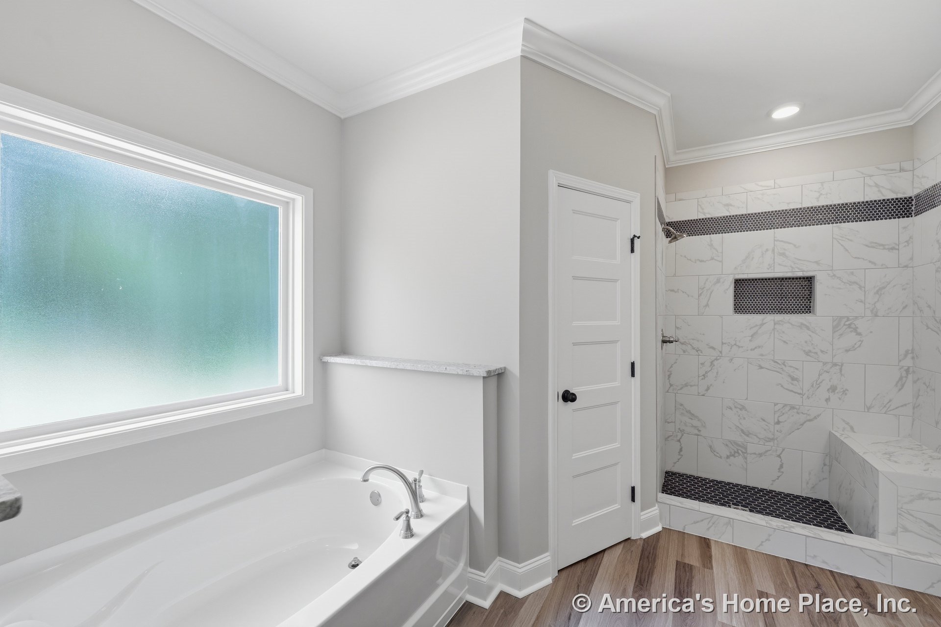 Soaking bathtub beside walk-in shower with marble-look tile, mosaic accents, built-in bench, frosted window, crown molding, recessed lighting, wood-look flooring, and white trim.