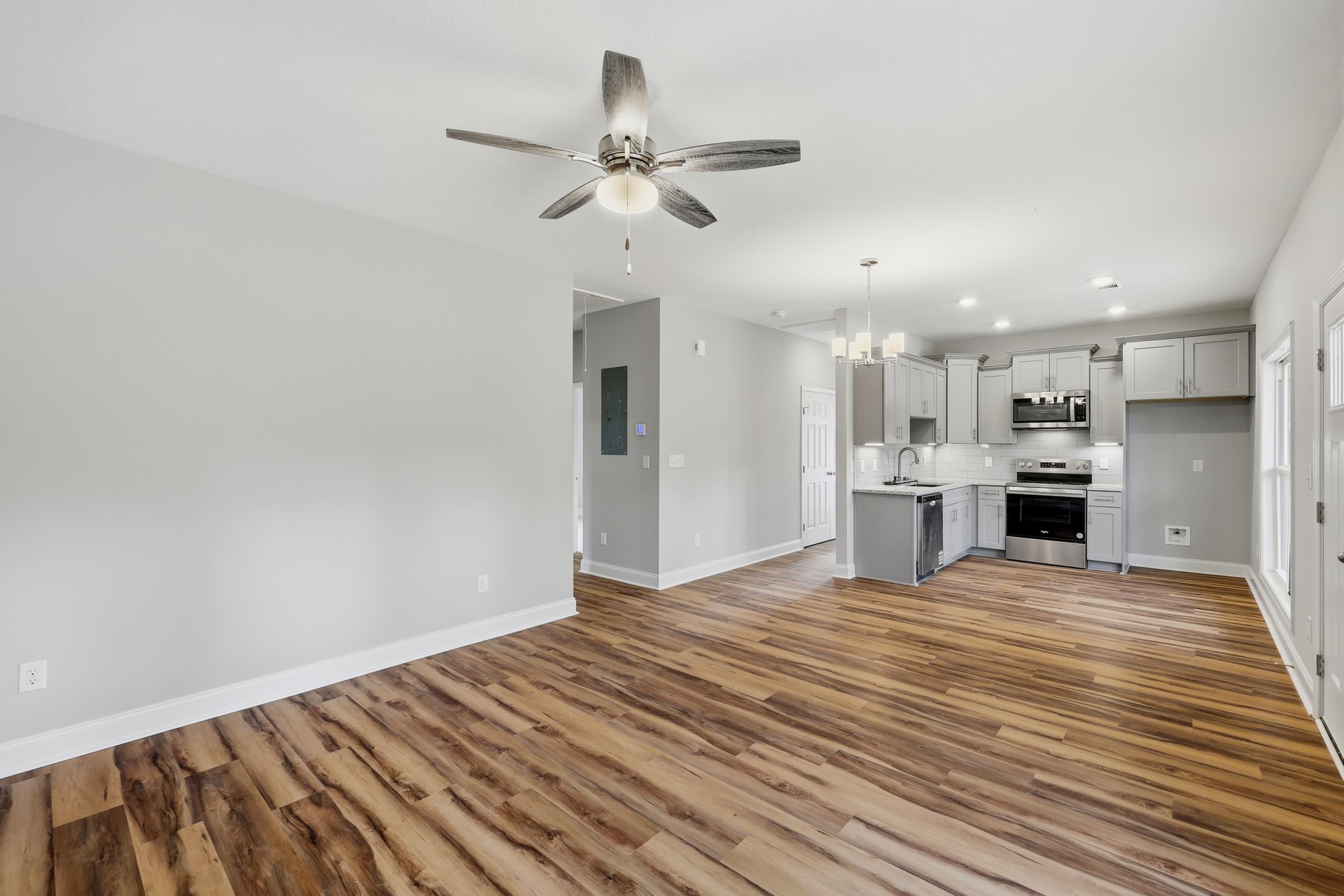 Open living space featuring wood flooring, white plaster walls, ceiling fan with light fixture, stainless steel stove with black door, and built-in microwave.