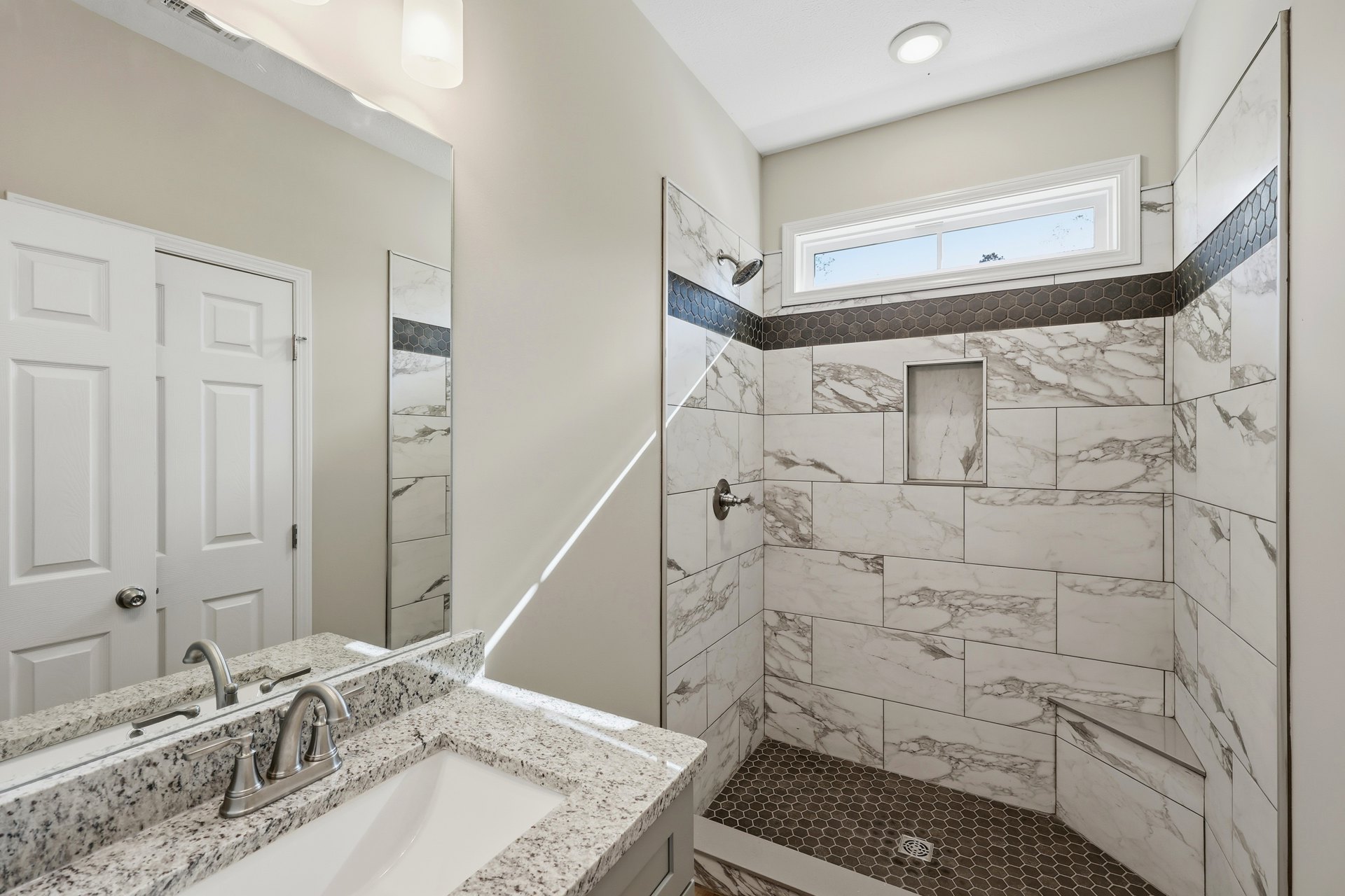 White marble tile walls, chrome faucet and handle, rectangular sink, glass shower enclosure, recessed ceiling light