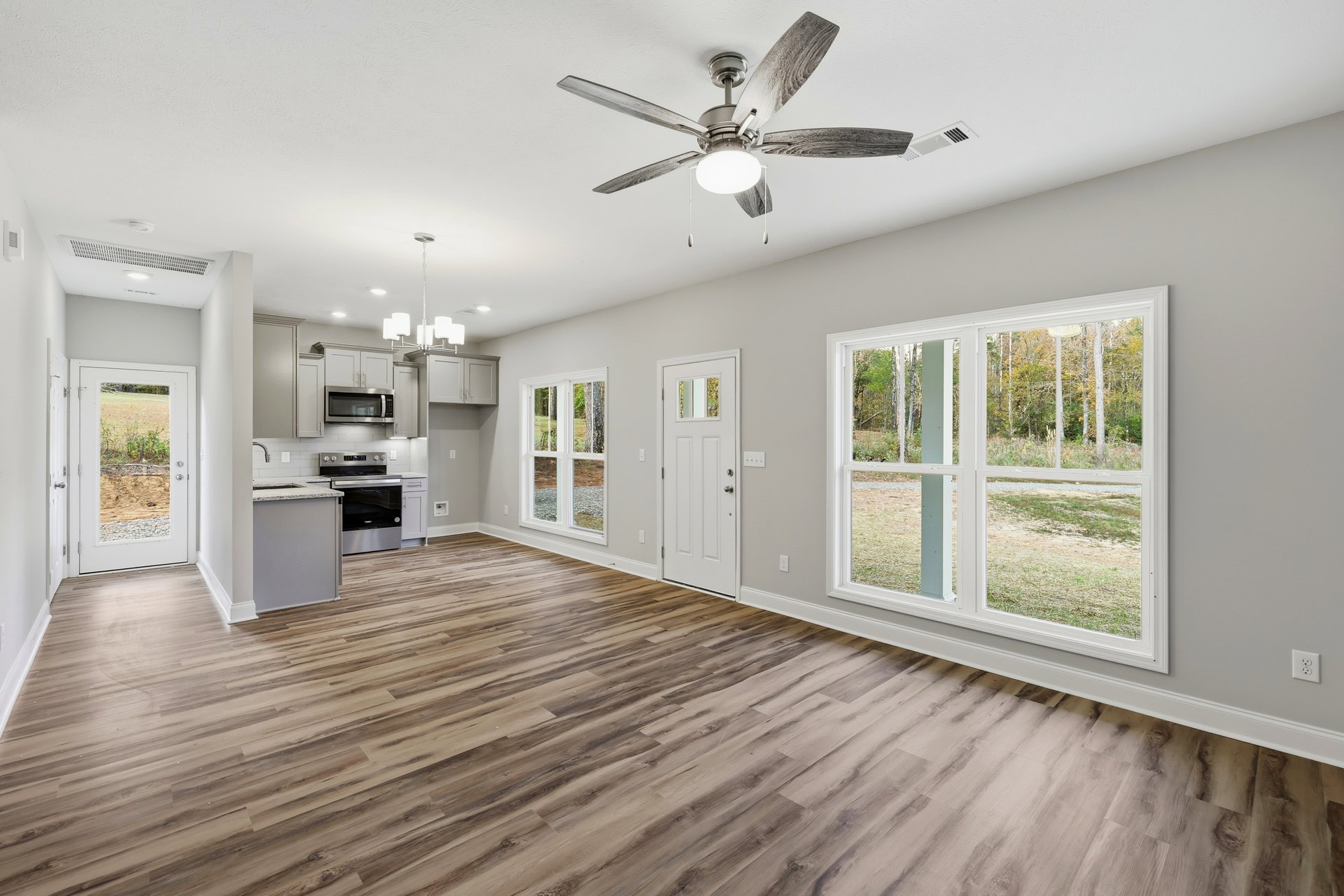Open-concept room featuring wood laminate flooring, white doors, ceiling fan with integrated light, microwave oven, plaster walls, and large window overlooking a grassy field.