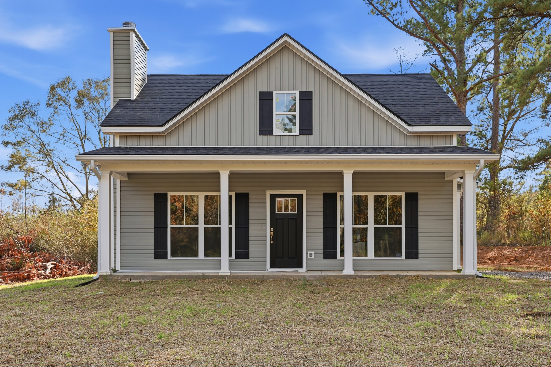 Modern house with black roof and black front door featuring glass panel, white siding, large windows with stickers, green lawn, and mature trees in front yard