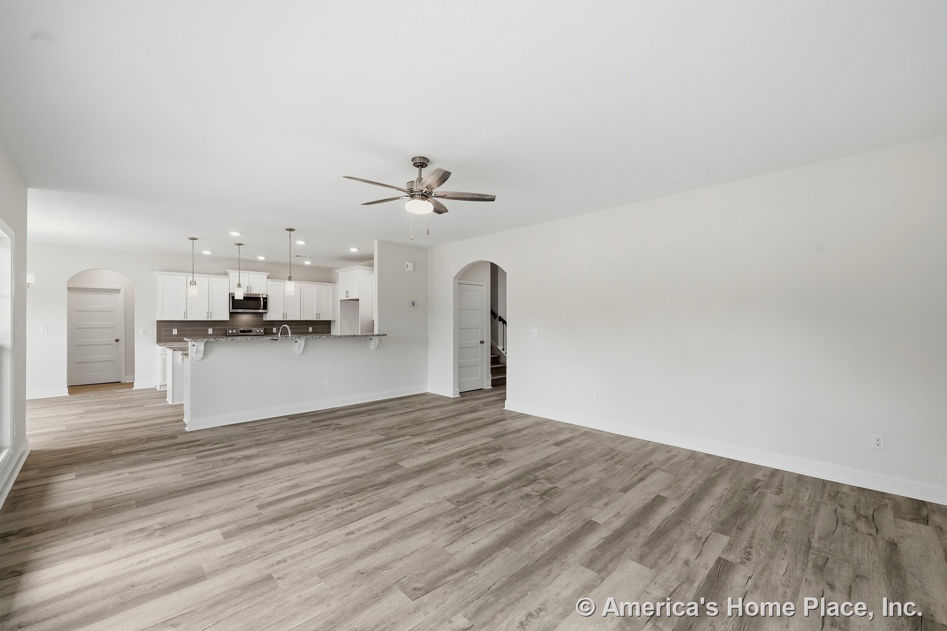 Open concept living area with wood-look plank flooring, kitchen featuring white shaker cabinets, granite countertops, stainless steel appliances, pendant lights above bar seating