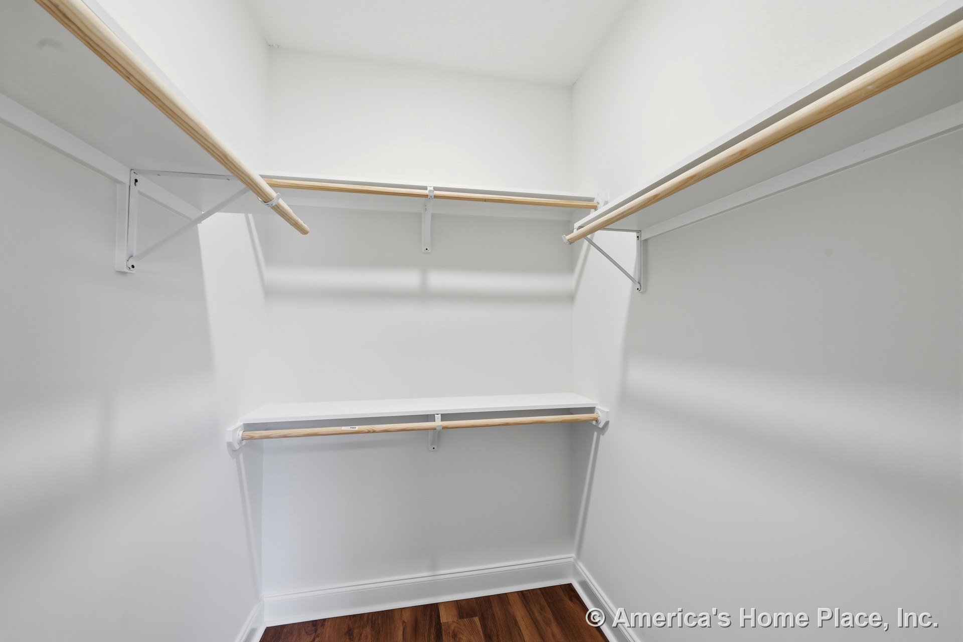 Walk-in closet with built-in wooden hanging rods, white shelving, white walls, wood-look flooring, open layout, and white trim.
