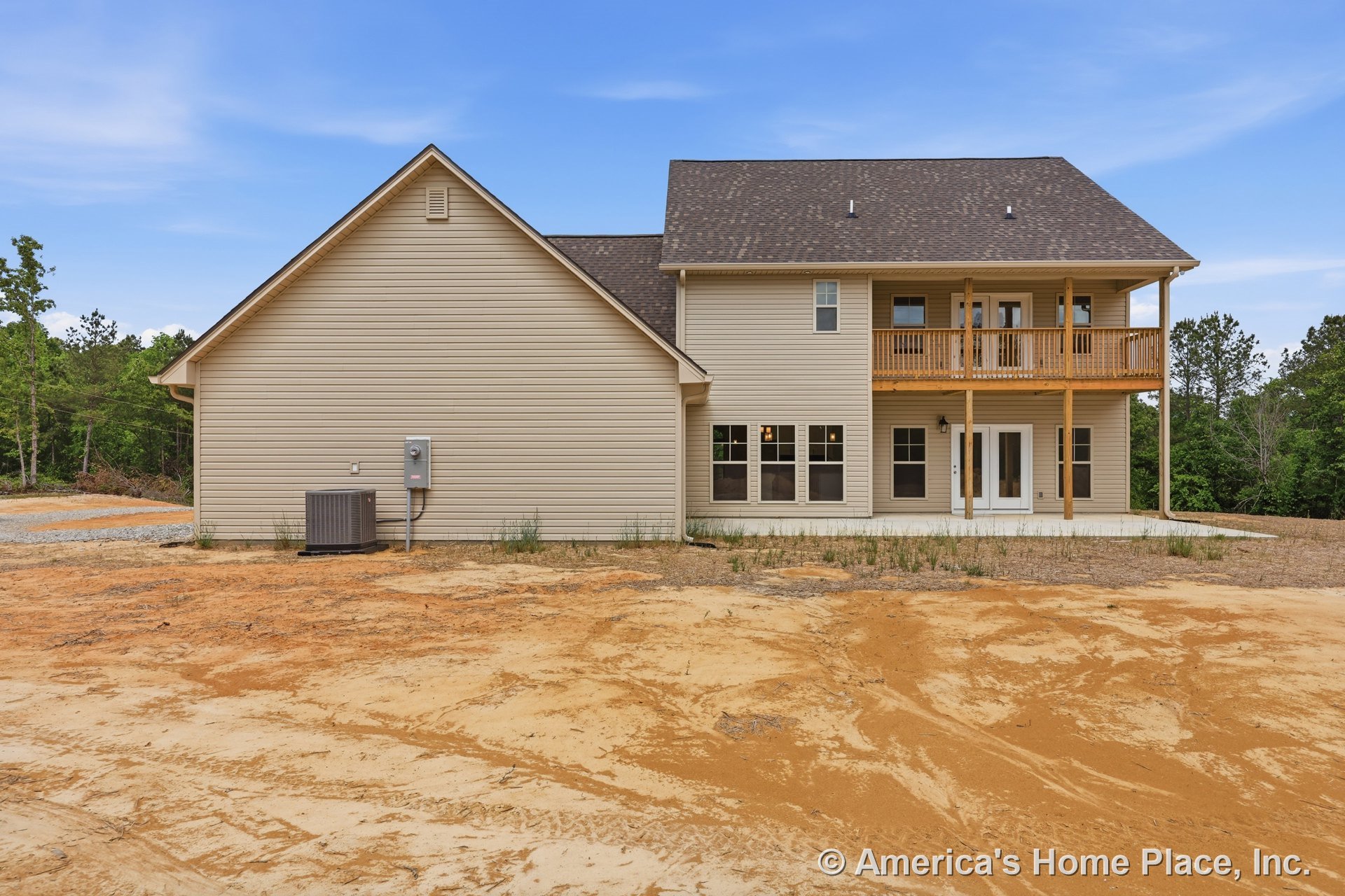 Beige vinyl siding exterior with gabled roof, covered upper balcony featuring wood railing, multiple large windows, concrete patio, double doors, outdoor lighting, white trim, and