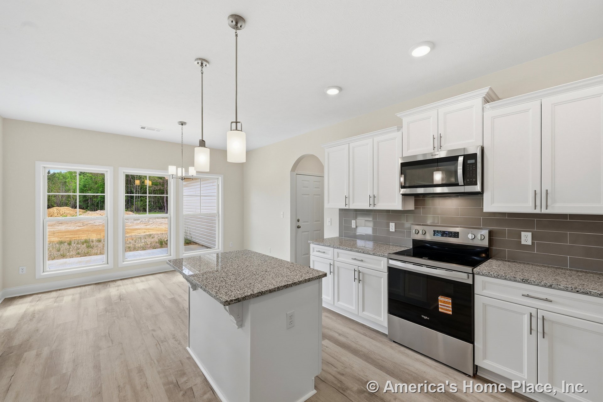 White shaker cabinets and granite countertops surround a central kitchen island, complemented by gray subway tile backsplash, stainless steel oven and built-in microwave, pendant