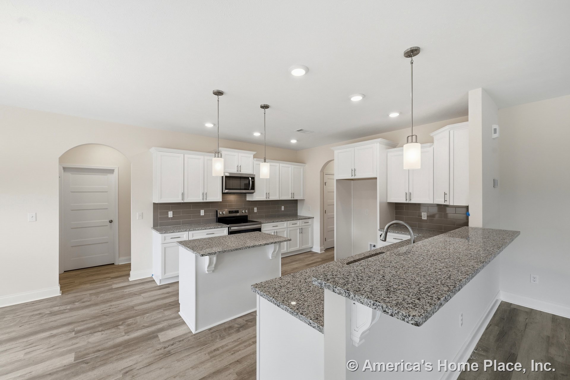 White shaker cabinets, granite countertops, gray subway tile backsplash, stainless steel appliances, pendant and recessed lighting, wood-look flooring, kitchen island with