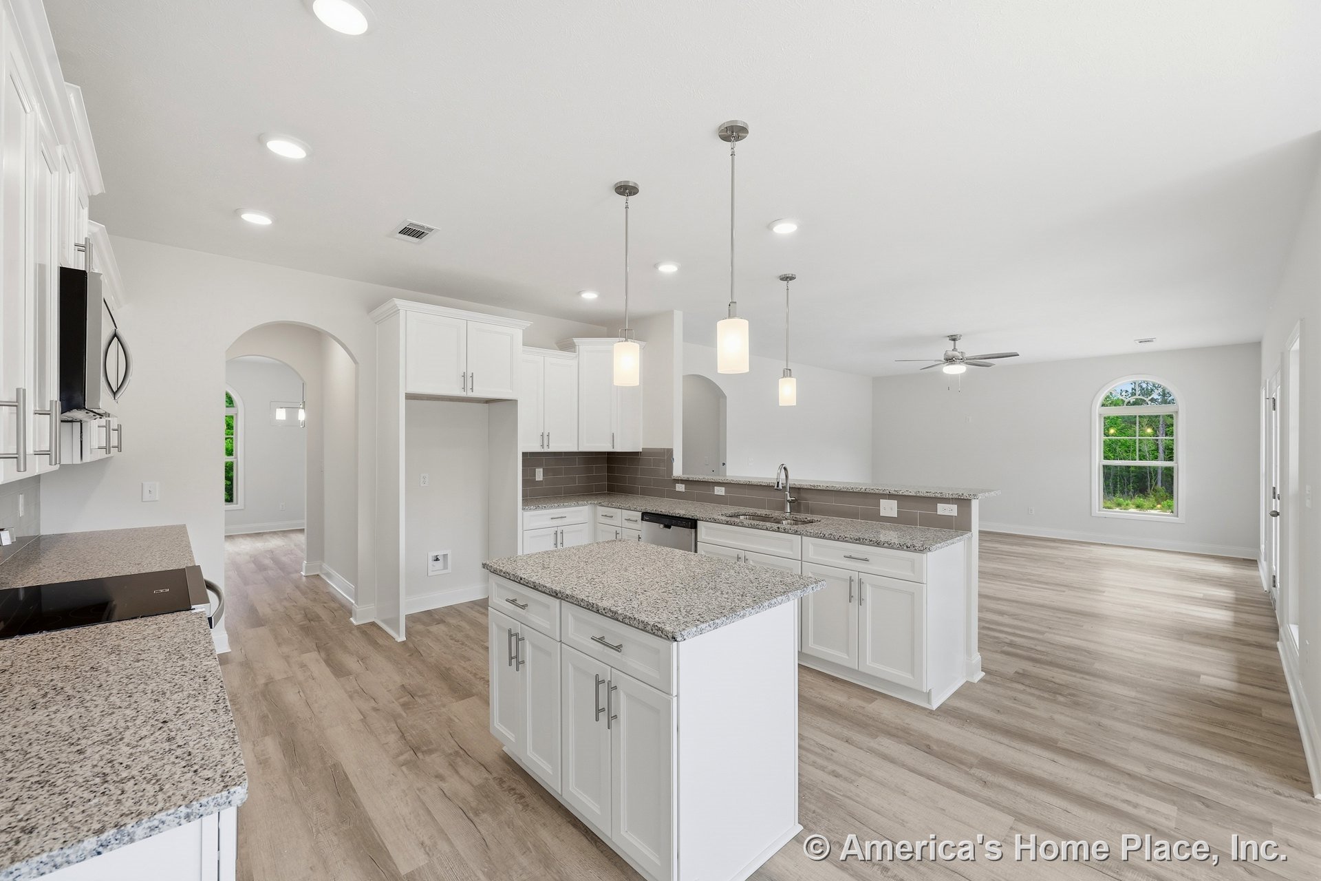 White shaker kitchen cabinets with granite countertops and tile backsplash, pendant lights above central island, wood-look plank flooring throughout open layout, arched doorway