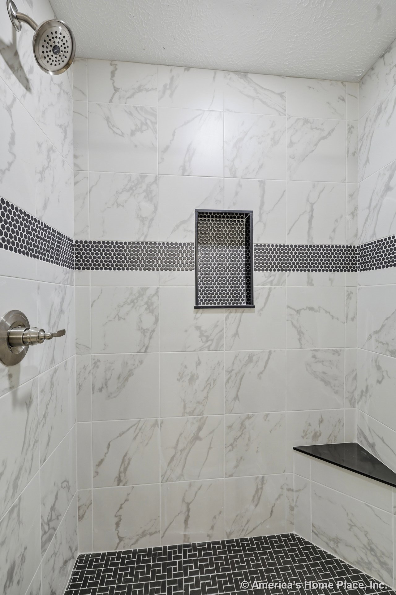 Marble-look ceramic wall tile with a black penny tile accent band, built-in shower niche and bench with matching black tile, patterned black tile floor, brushed nickel shower