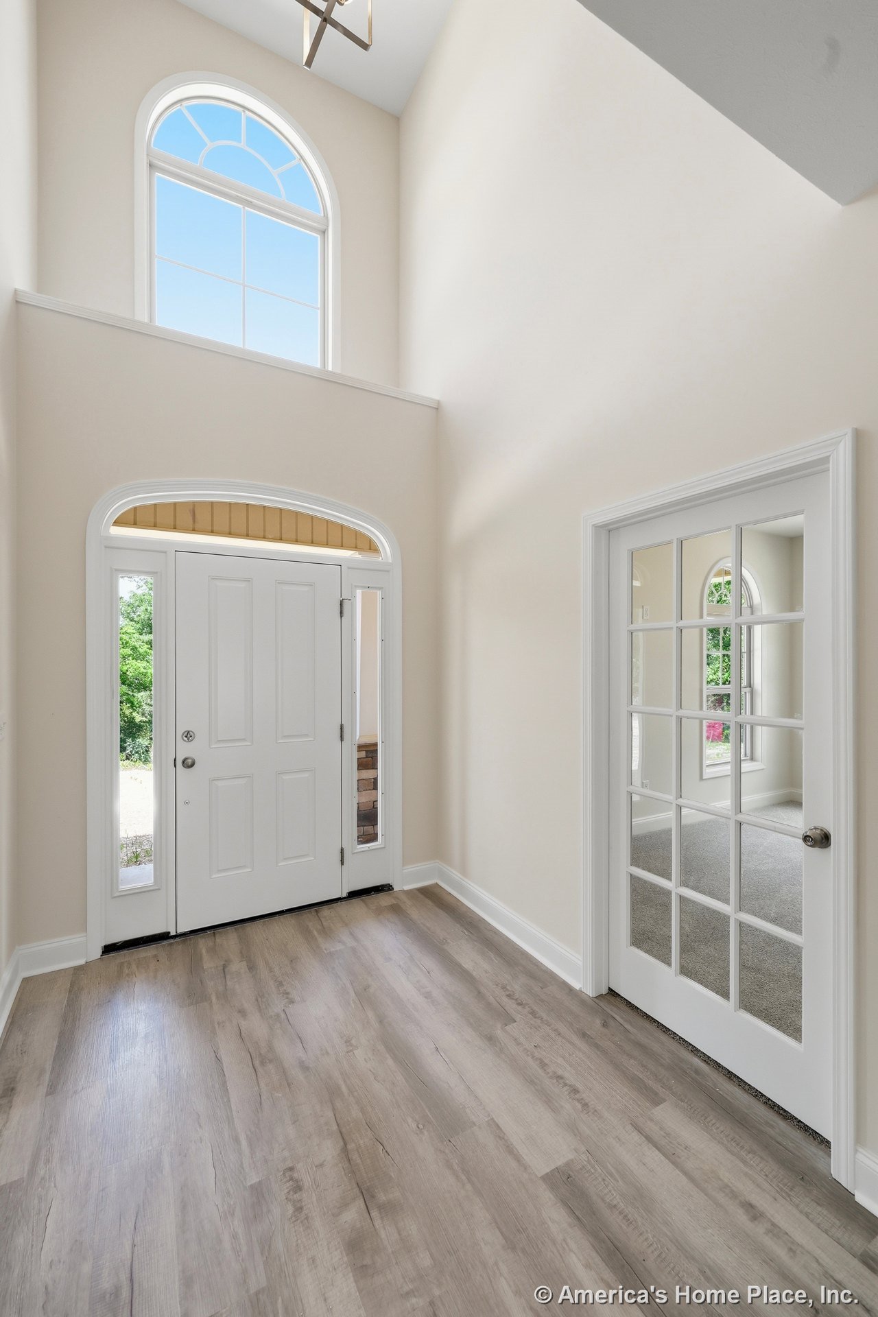 Double-height foyer with arched transom window above white front door with sidelights, glass-paneled office door, light wood flooring, and neutral wall trim.