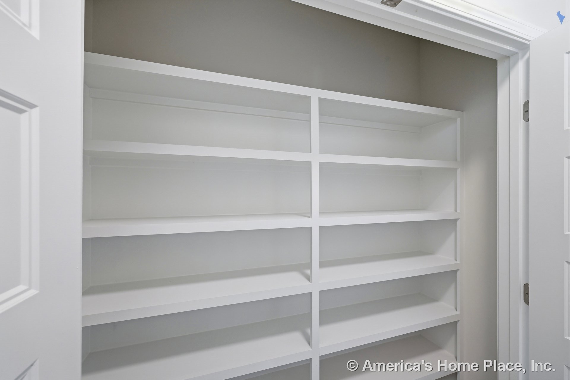 Built-in white painted shelving and cabinetry line the walk-in pantry closet, offering organized storage with multiple open shelves, trimmed door opening, and neutral wall color.