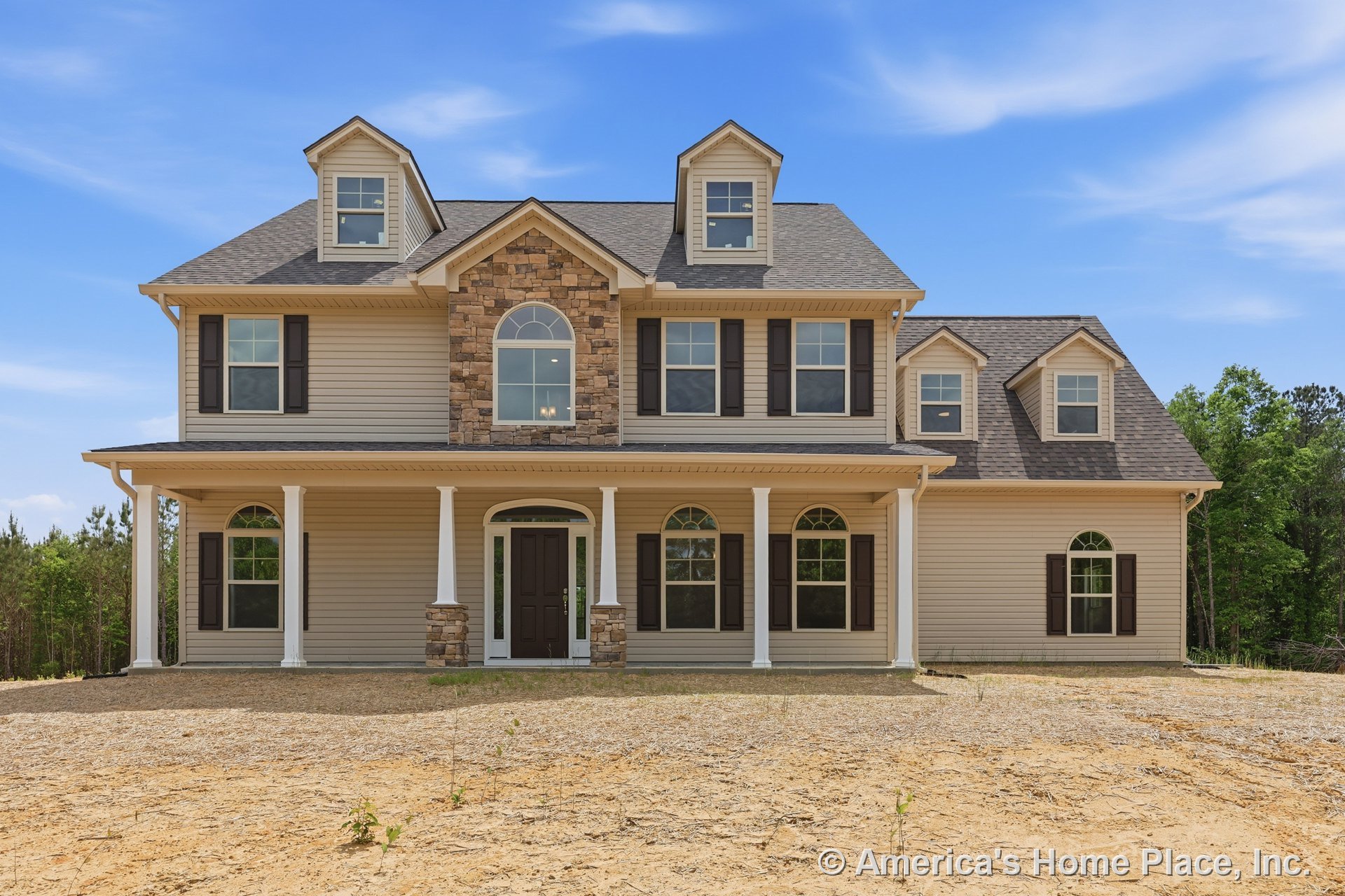 Two-story home exterior with tan vinyl siding, stone accent wall, covered porch supported by columns, multiple dormer windows, arched windows with shutters, double front door, and