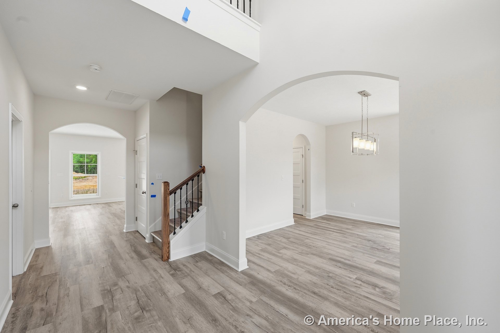 Wide plank wood-look flooring in foyer with arched doorways, staircase featuring iron balusters, large hallway window, modern ceiling light fixture, white trim and baseboards, and