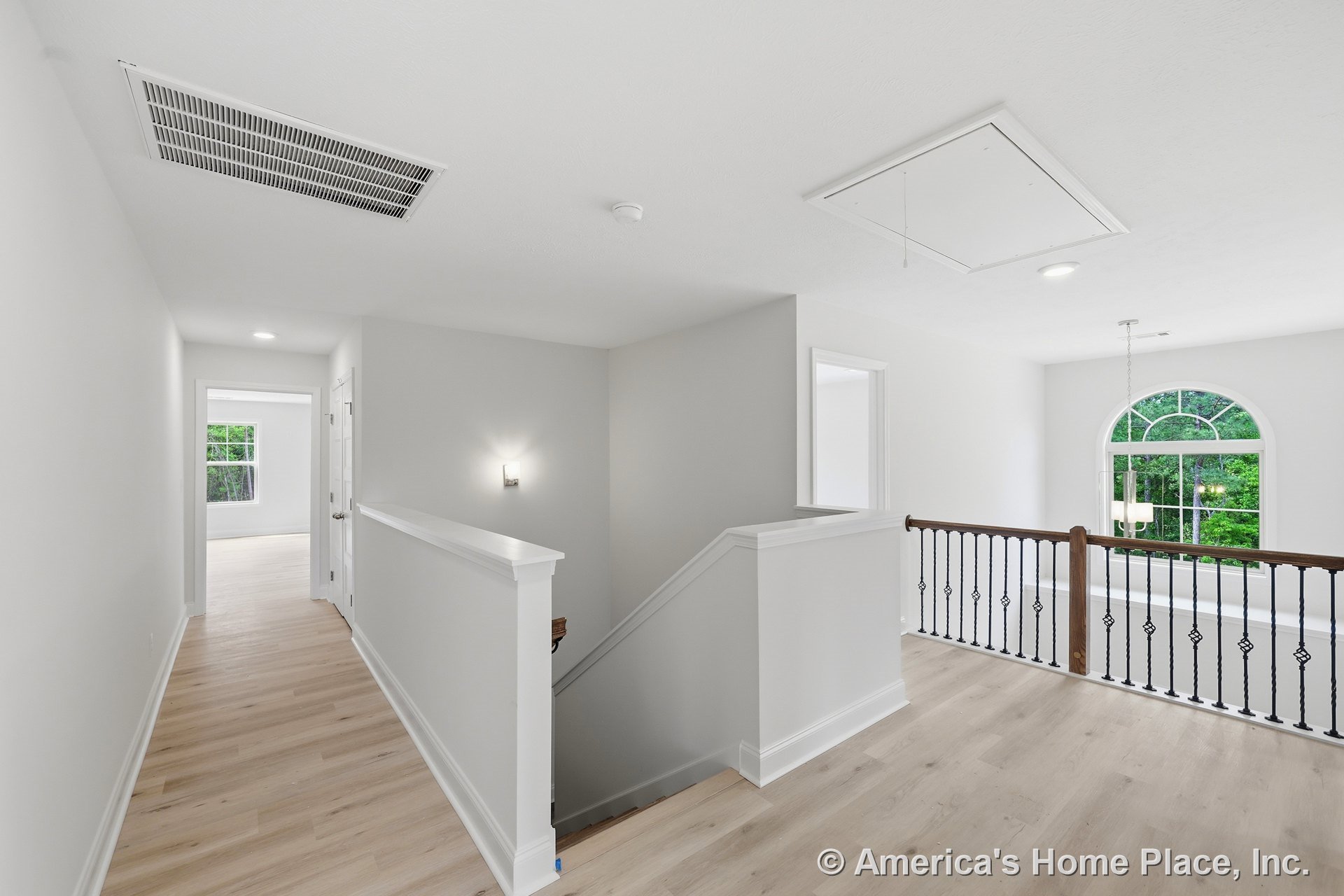 Upstairs landing with light wood flooring, white stair trim, decorative iron railing, large arched window, recessed ceiling lights, wall sconce lighting, neutral walls, ceiling