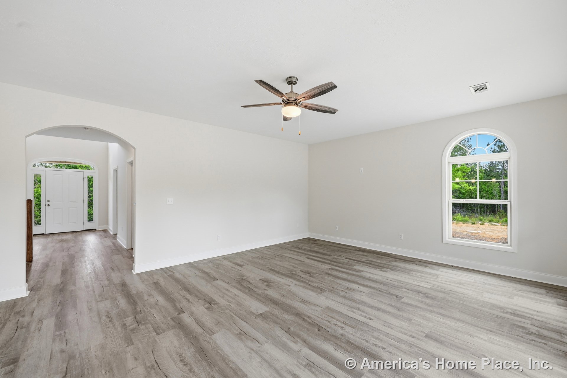 Light wood-look vinyl plank flooring, arched window with divided lights and white trim, ceiling fan with integrated light fixture, arched entryway, front door with sidelights