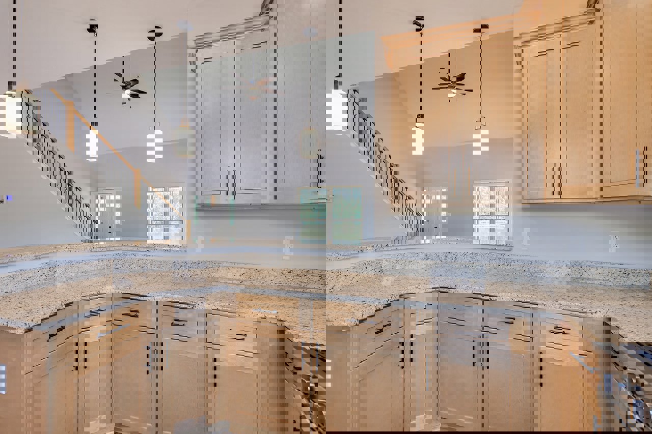 Marble countertop kitchen with white cabinetry, stainless steel sink and faucet, window overlooking trees, staircase with pendant lights, close-up of wood cabinet and door