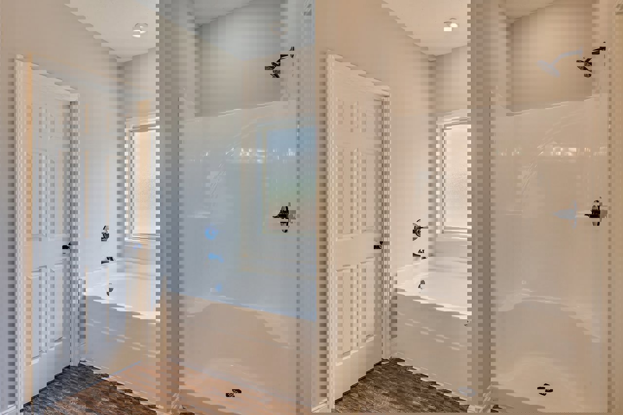 Bathroom with white bathtub and glass-enclosed shower, black hardware on white door and shower handle, tile walls, window above tub, curved shower head.