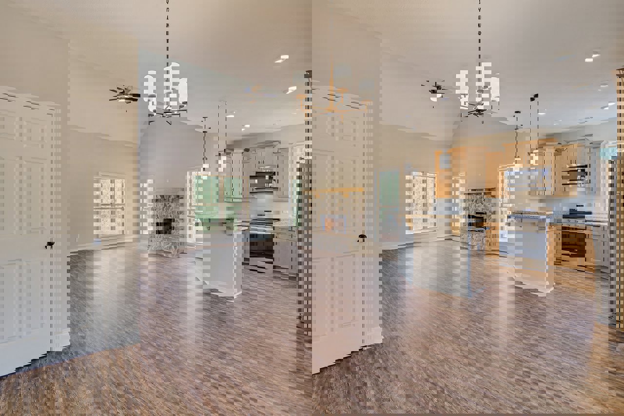 Spacious open floor plan featuring hardwood flooring, central fireplace with glass door, white framed window, white door with black knob, modern cabinetry, and ceiling details