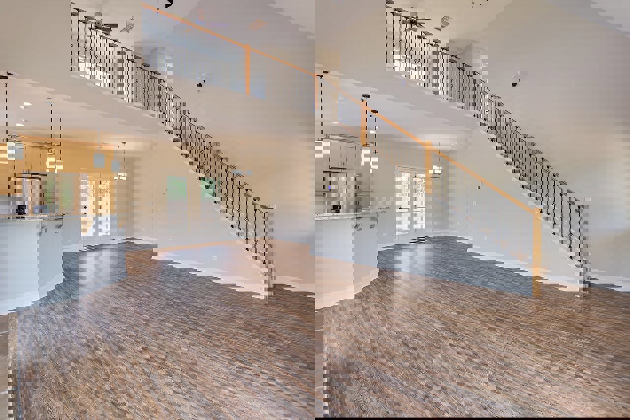 Spacious interior featuring hardwood floors, metal-railed staircase, glass-paneled double doors, and stainless steel refrigerator