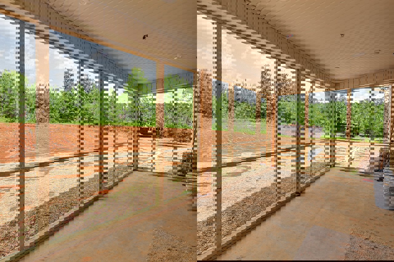 Spacious room featuring a large floor-to-ceiling window overlooking a dirt field, light wood flooring, and exposed wooden post near grey utility buckets