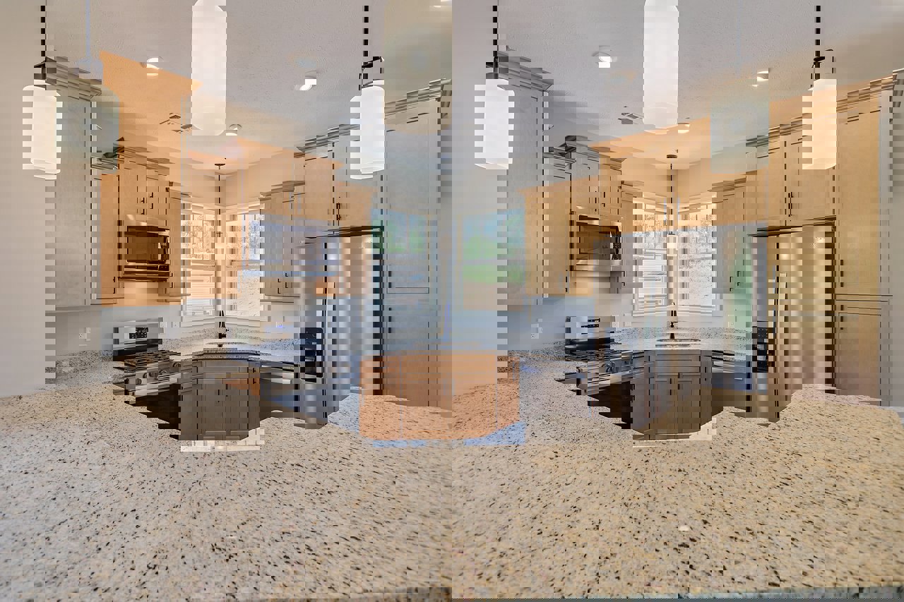 Granite countertops, stainless steel refrigerator with glass door, open microwave, stove and oven, white under-cabinet lighting, window overlooking outdoors, wood cabinetry and