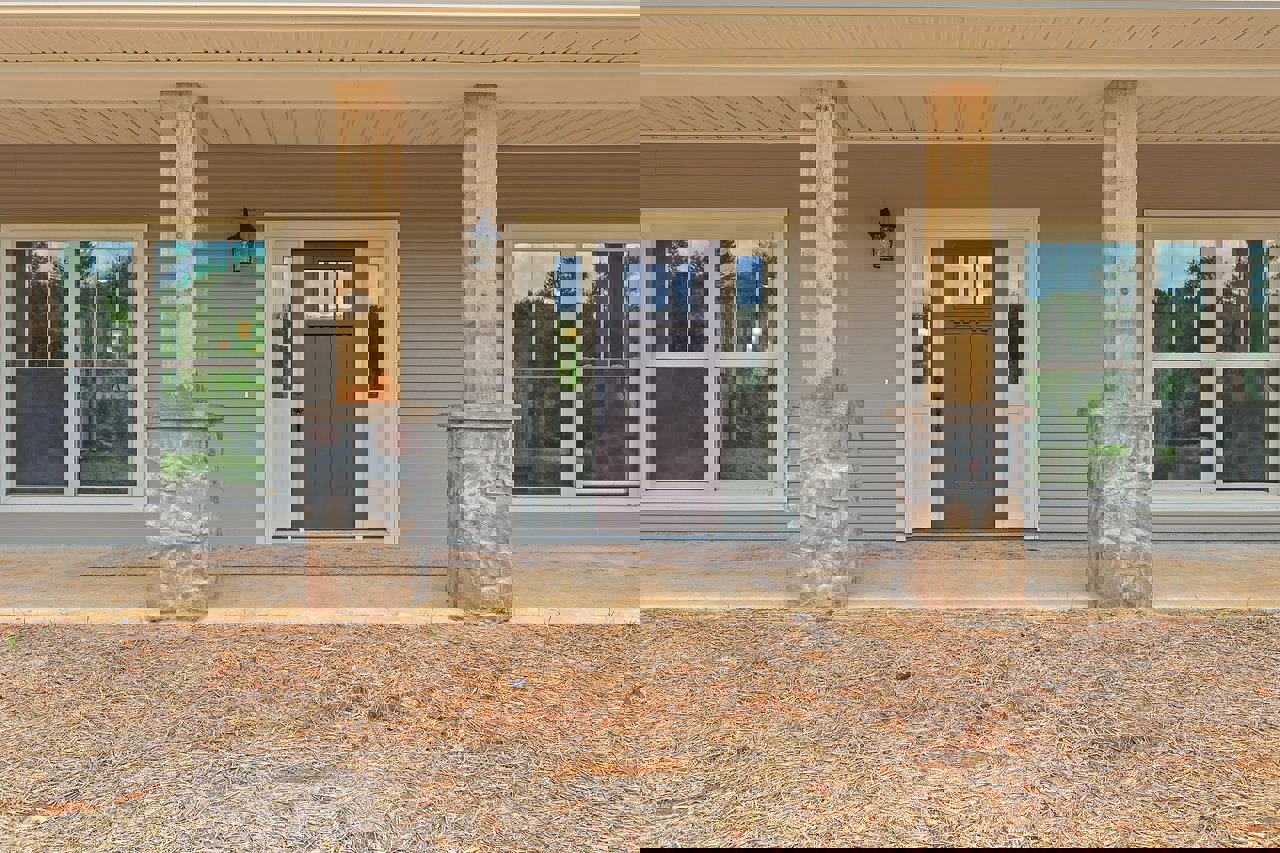 Front porch with brown door featuring glass window, adjacent white-framed window, bird standing on concrete ground