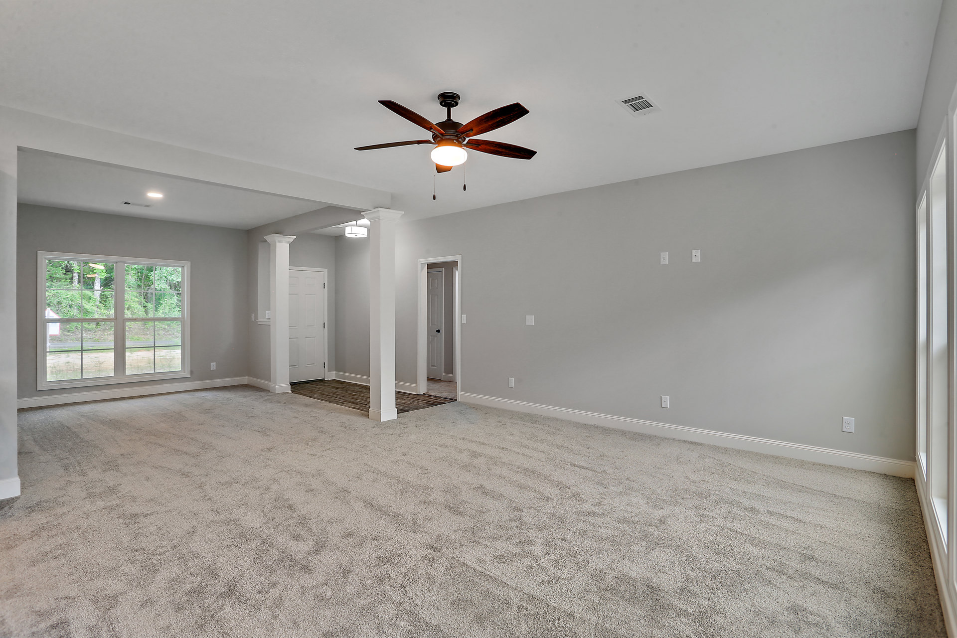 Carpeted room with white walls, ceiling fan with light fixture, window showing trees outside, door featuring a hole in the center