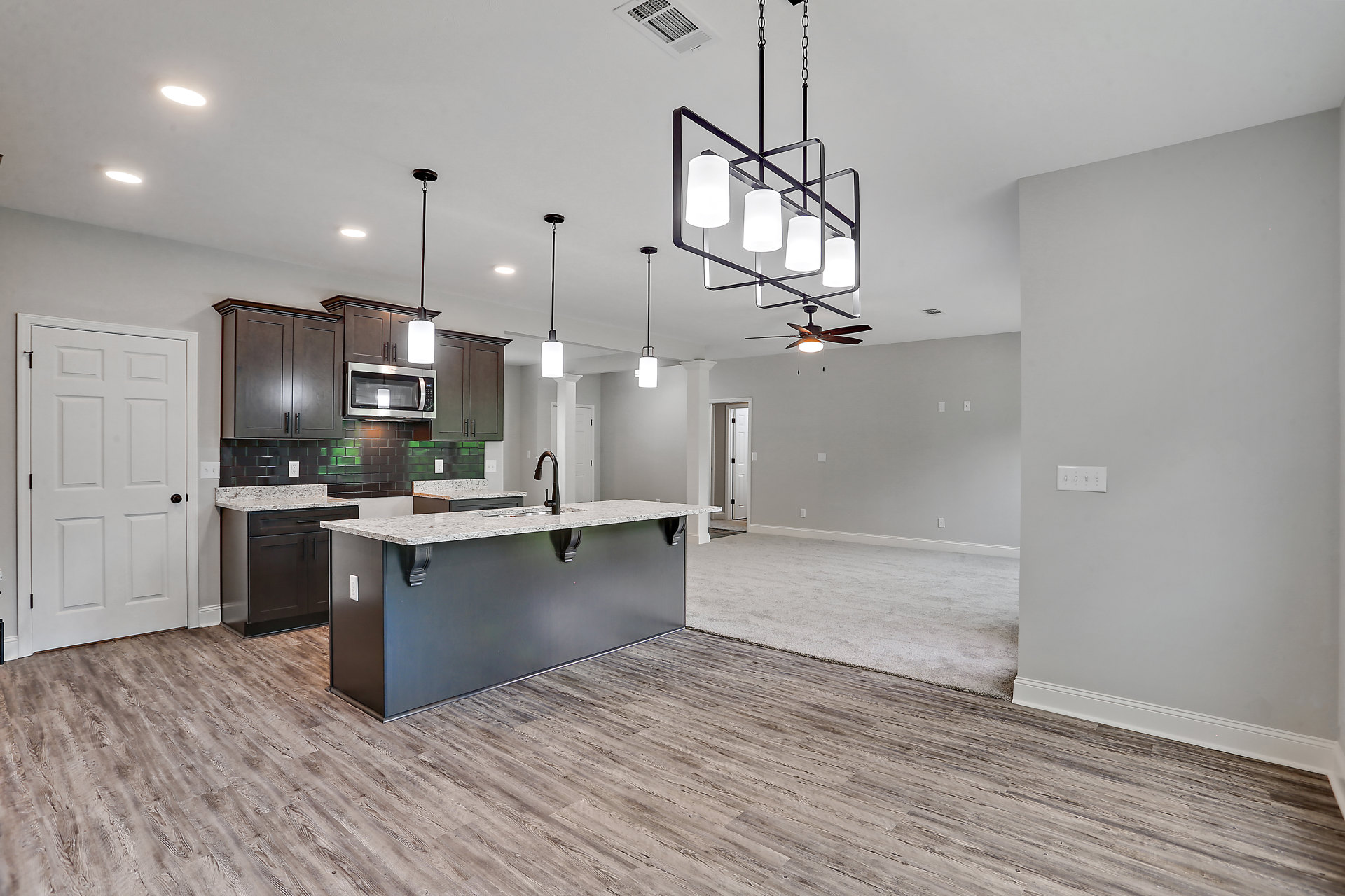 Open kitchen and living room featuring a central island with sink, white cabinetry, stainless steel microwave, white door with black handle, and a chandelier with four lamps