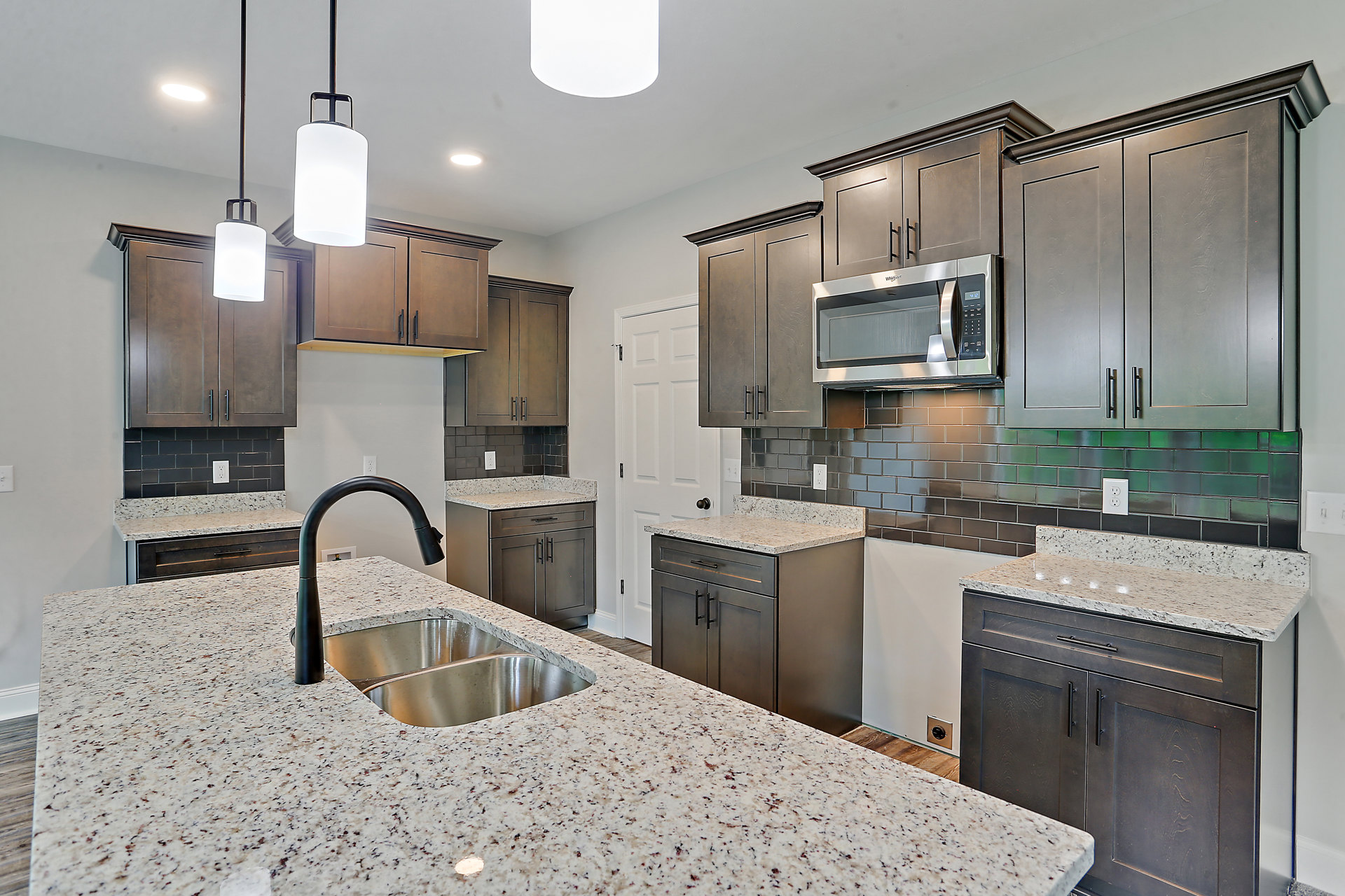 Granite countertops with white cabinets, stainless steel sink and black faucet, open microwave door, marble backsplash, modern kitchen appliances