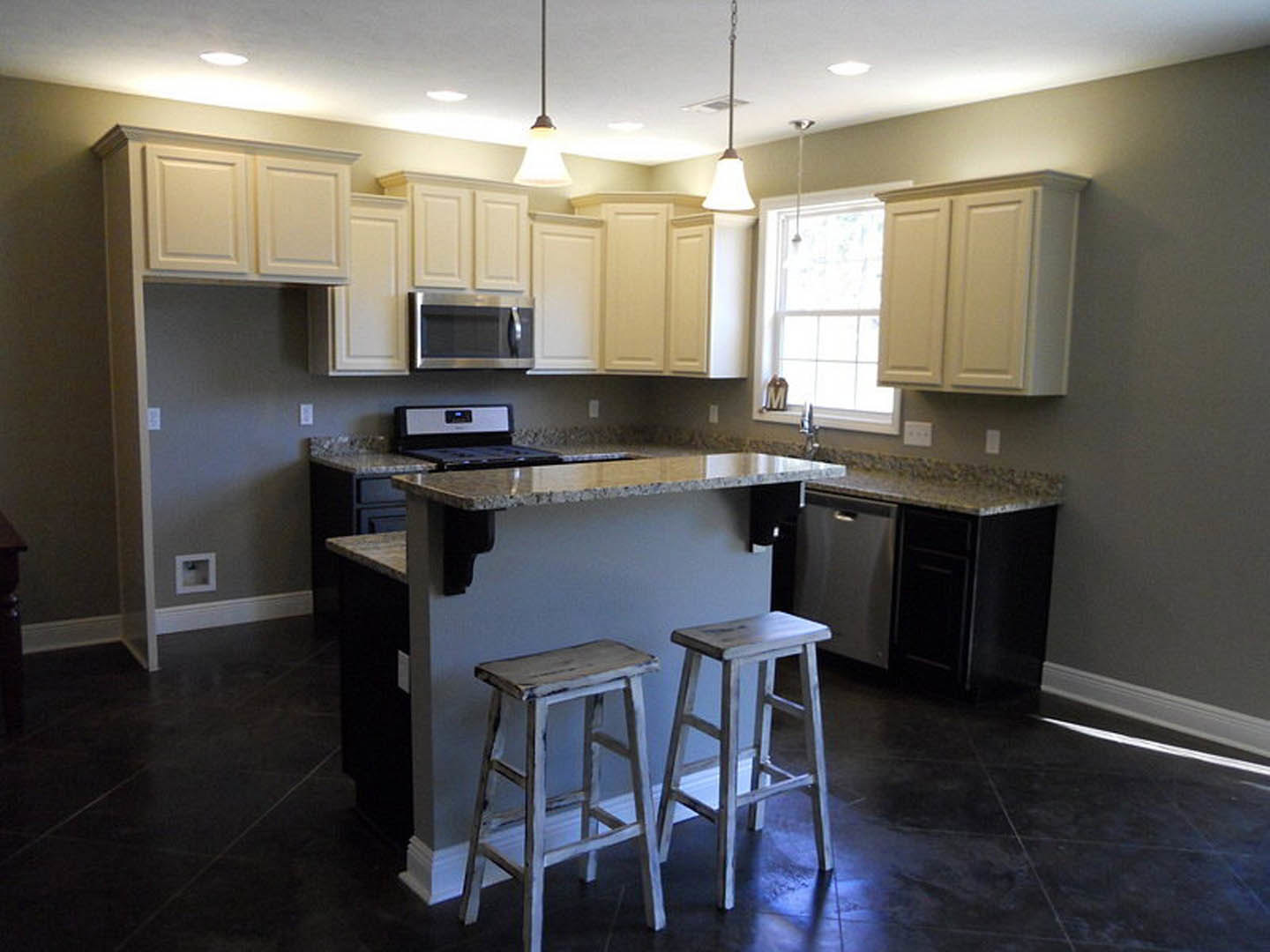 Modern kitchen featuring a central island bar with two wooden stools, white cabinetry, stainless steel appliances, light stone countertops, and a tile backsplash
