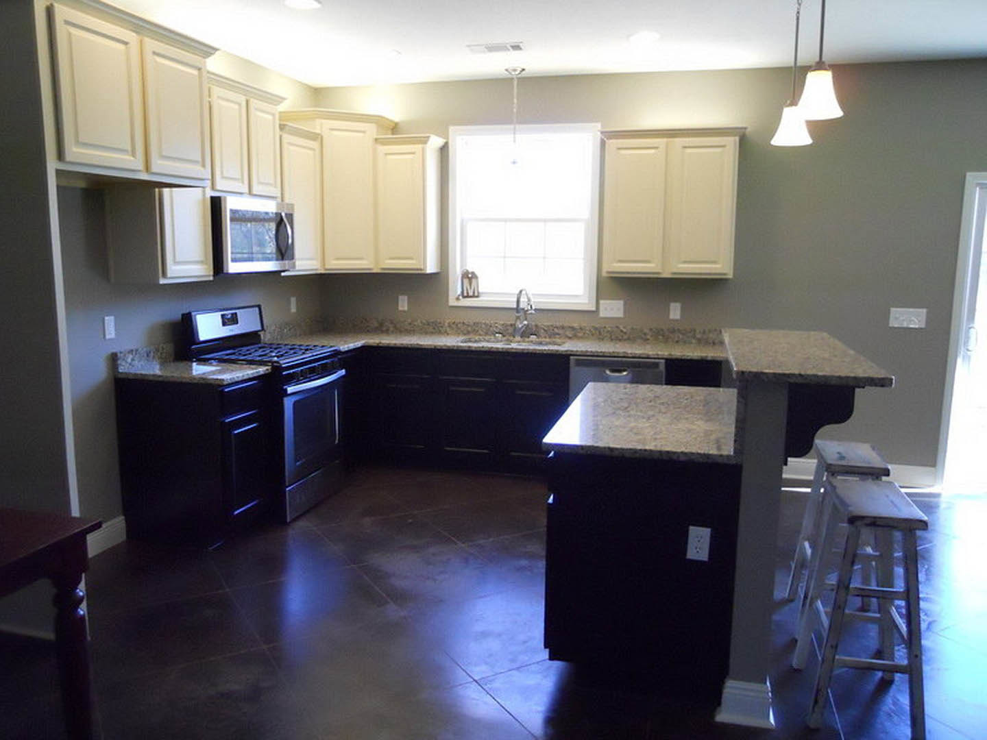 Granite countertops with wood cabinetry, stainless steel stove and microwave, sunlight streaming through window, white electrical outlet on backsplash