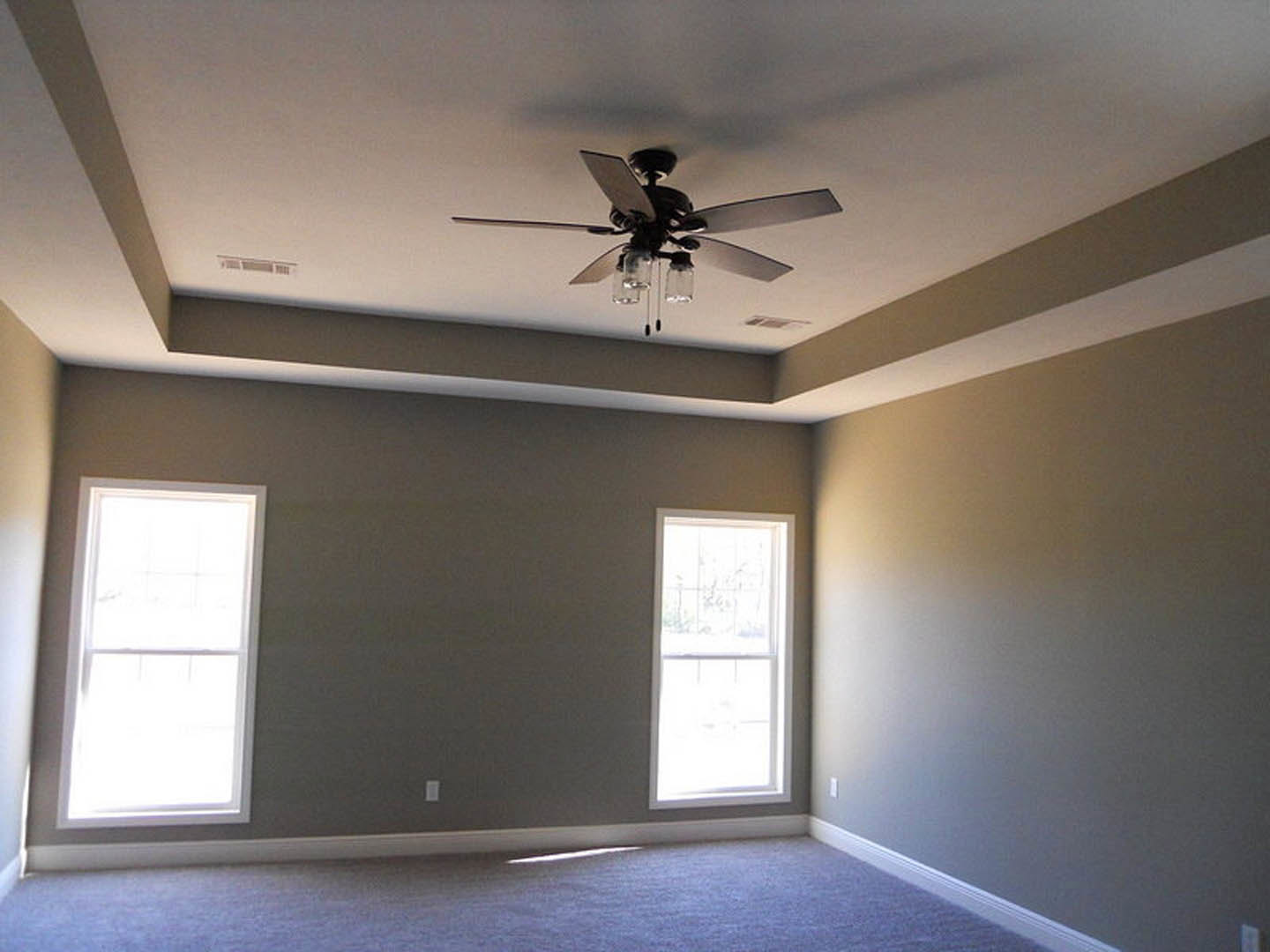 Ceiling fan with glass jar light fixtures above blue carpet, white-framed window, and plaster walls in a residential room
