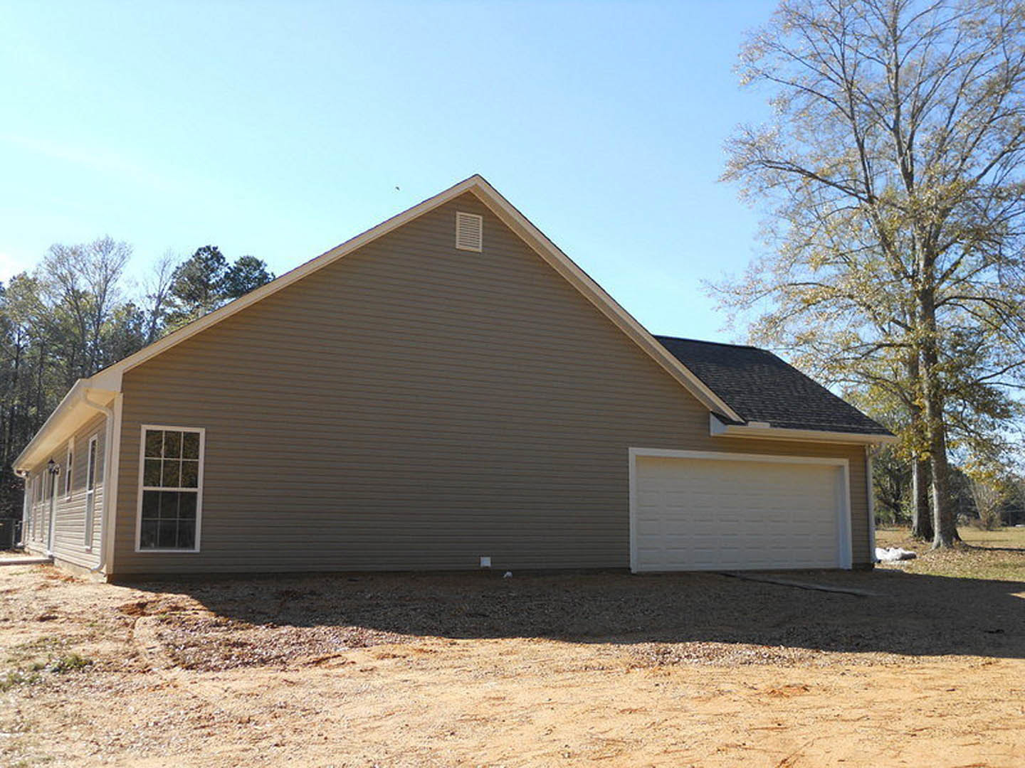 Two-story home with gray siding, white-trimmed windows, attached garage with paneled door, gabled roof, leafy tree in front yard