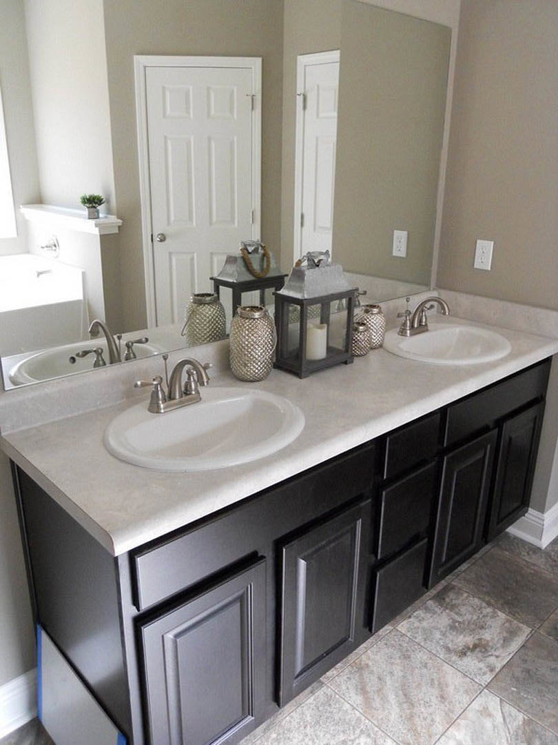 Bathroom with two rectangular sinks set in a stone countertop, chrome faucets, white cabinetry, silver vase, candle lantern, and white door with silver handle