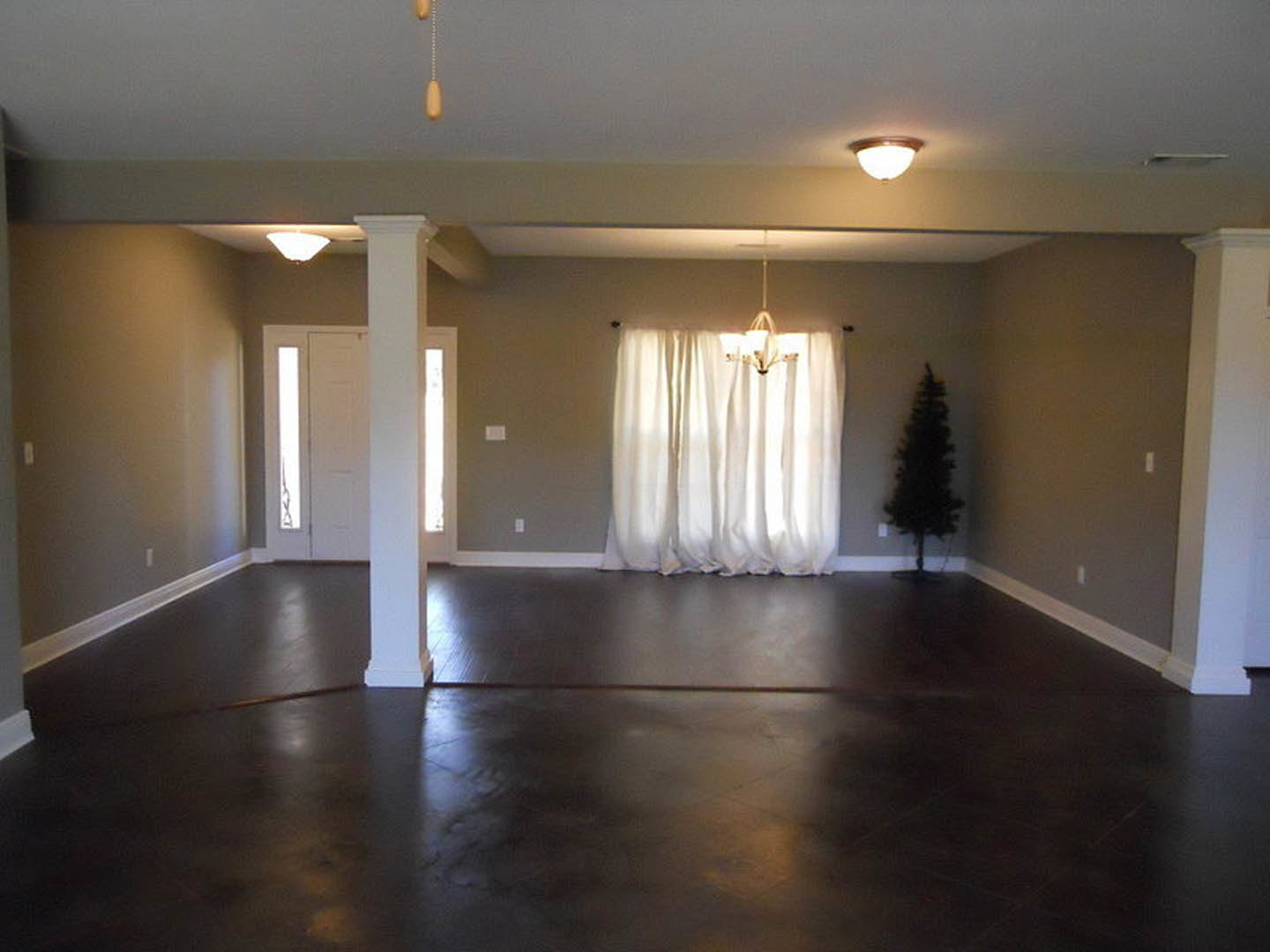White door with glass panels, dark laminate flooring, white curtains, chandelier, small indoor tree, plaster walls, natural light filtering through windows.
