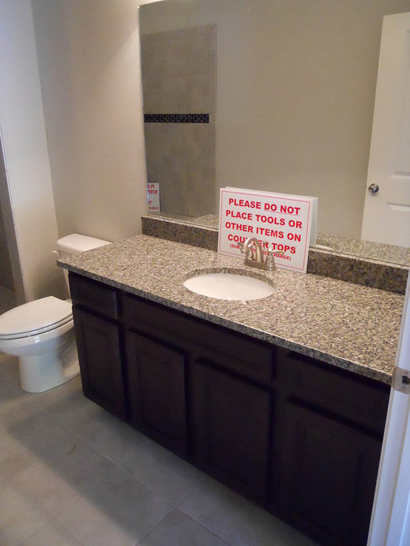 White porcelain sink and toilet in a bathroom with light tile walls, chrome faucet, and a small sign on the countertop