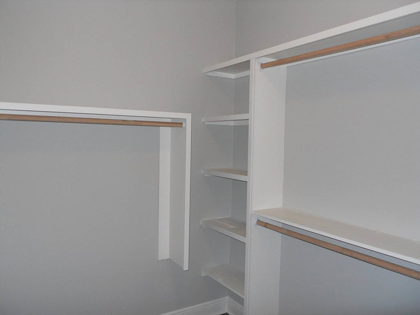 Walk-in closet with white walls, built-in shelves, and wooden hanging rods